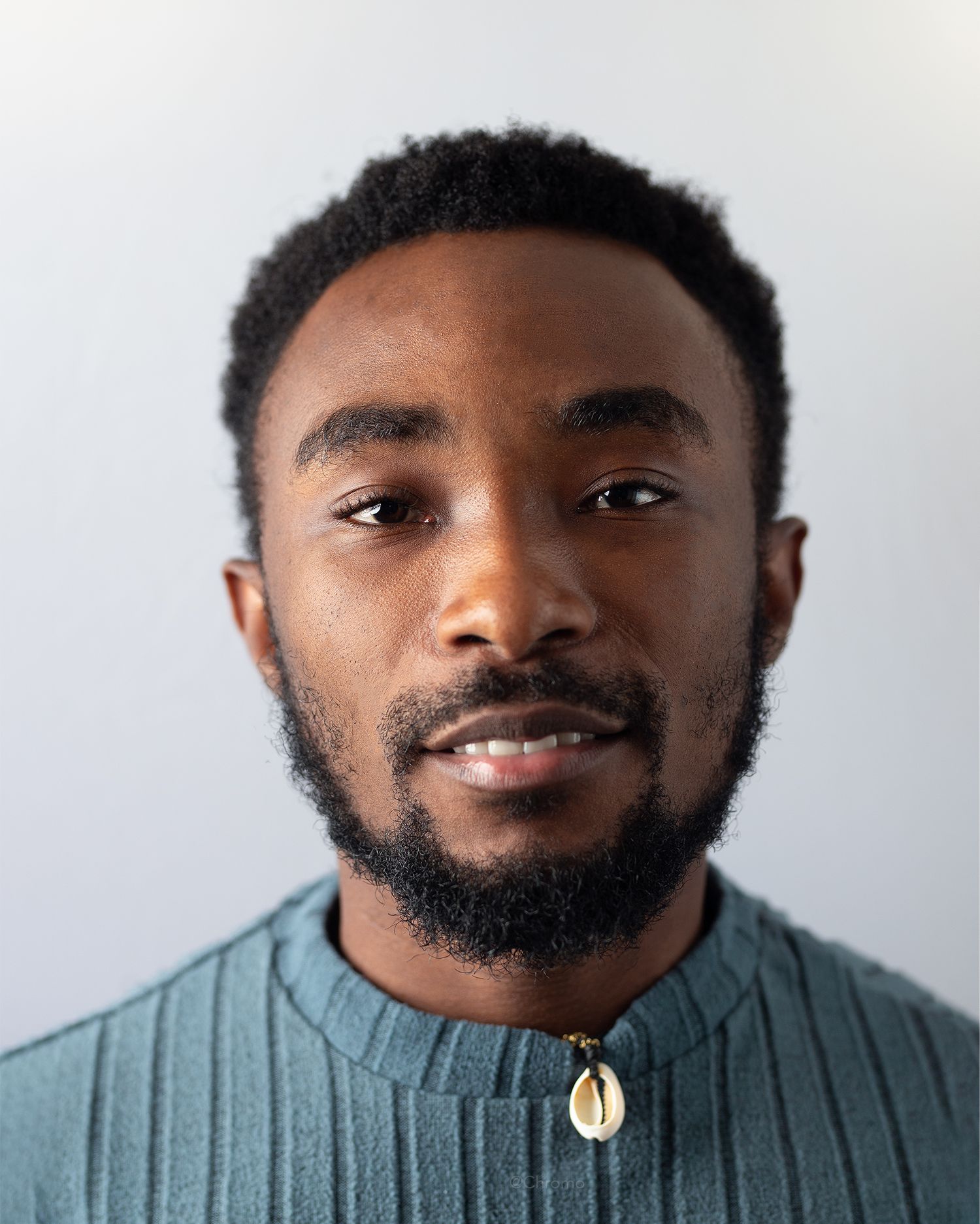 Professional headshot featuring green collared shirt and shell necklace against white background.