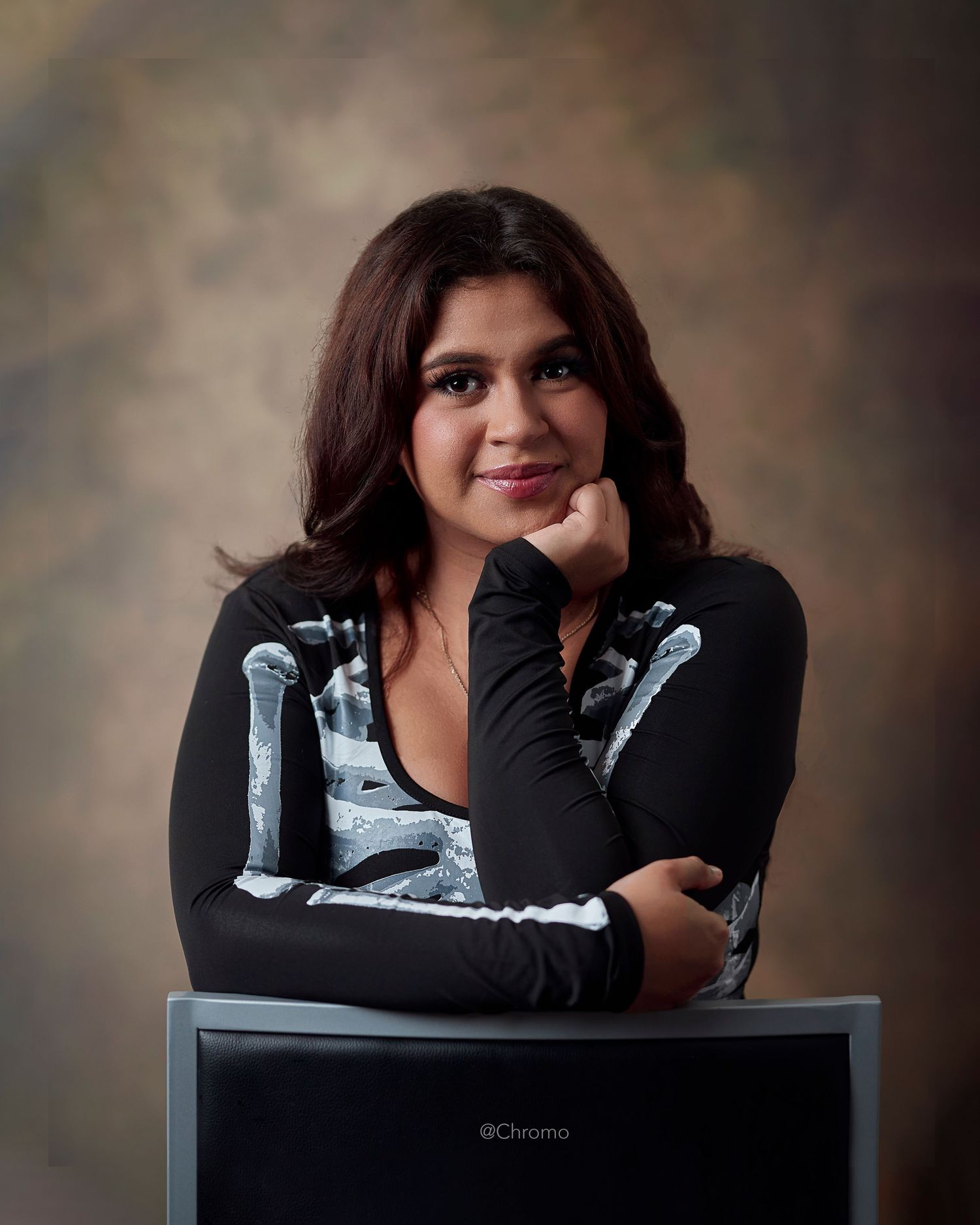 Studio portrait with person in black and white graphic long sleeve top leaning on dark surface.