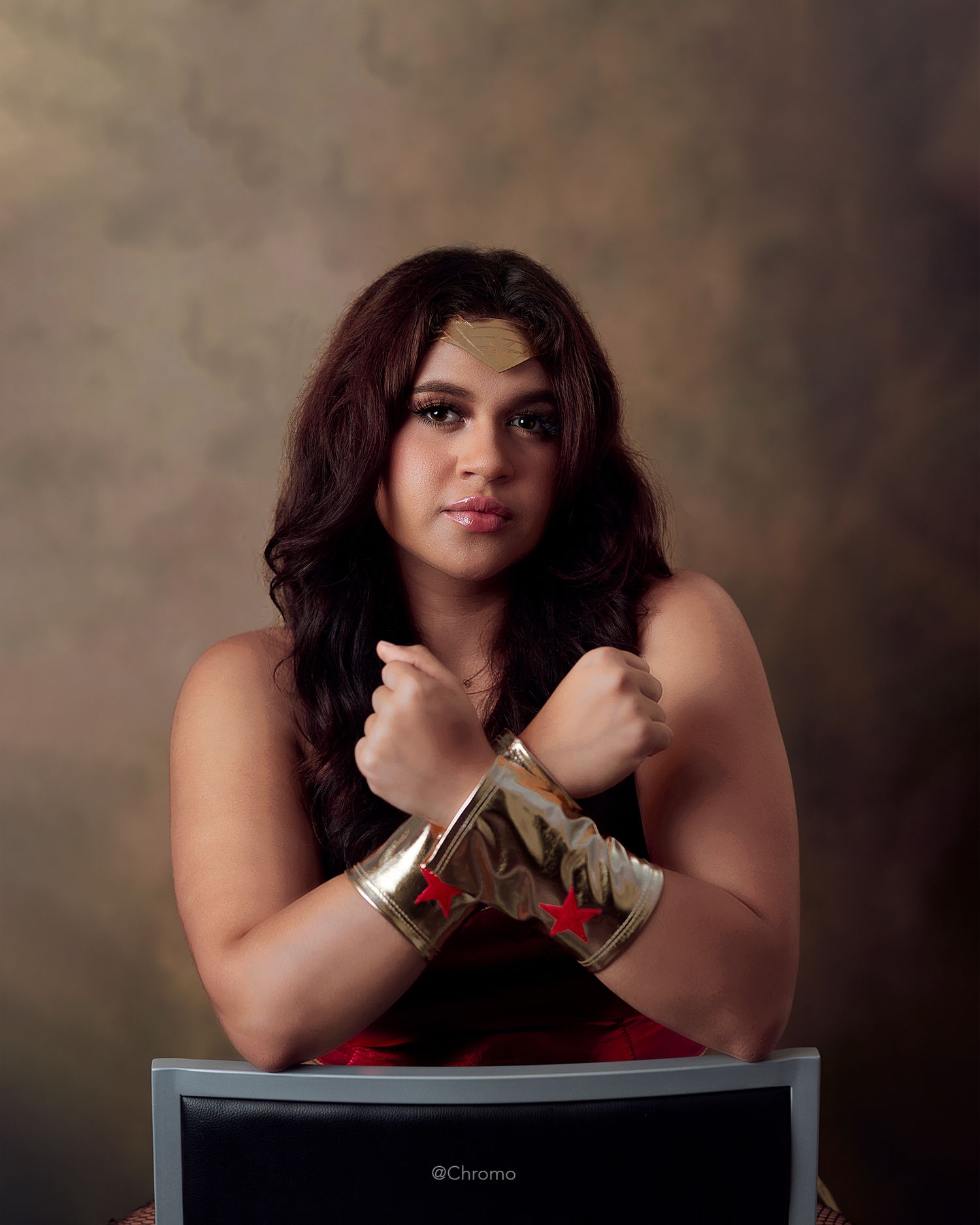 Studio portrait of person in red top wearing metallic arm cuffs against brown backdrop.