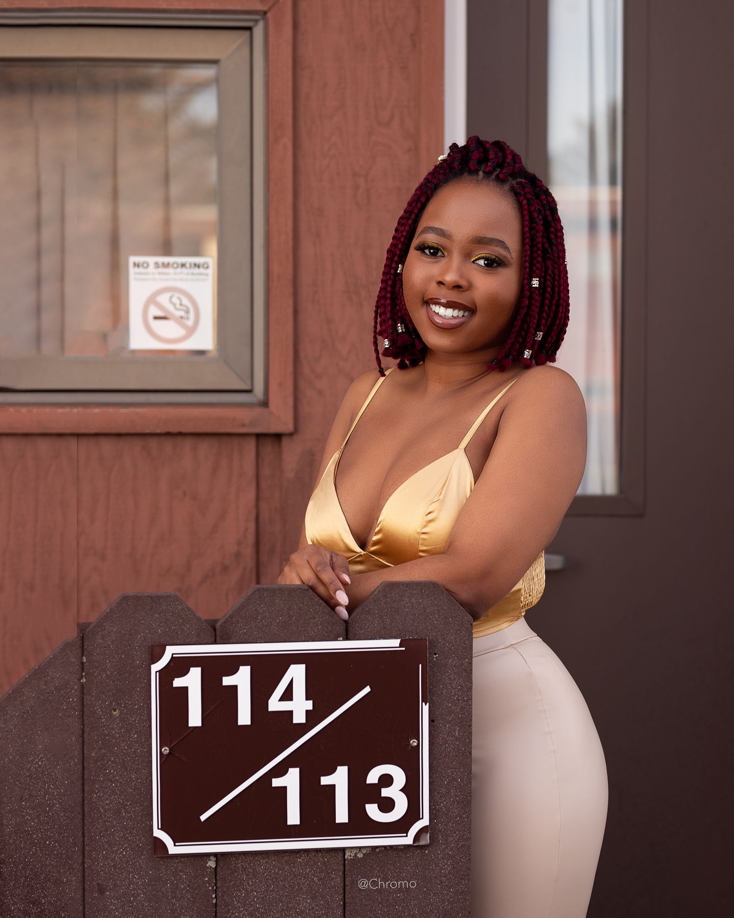 Casual portrait next to room number 114/113 sign wearing a gold top.