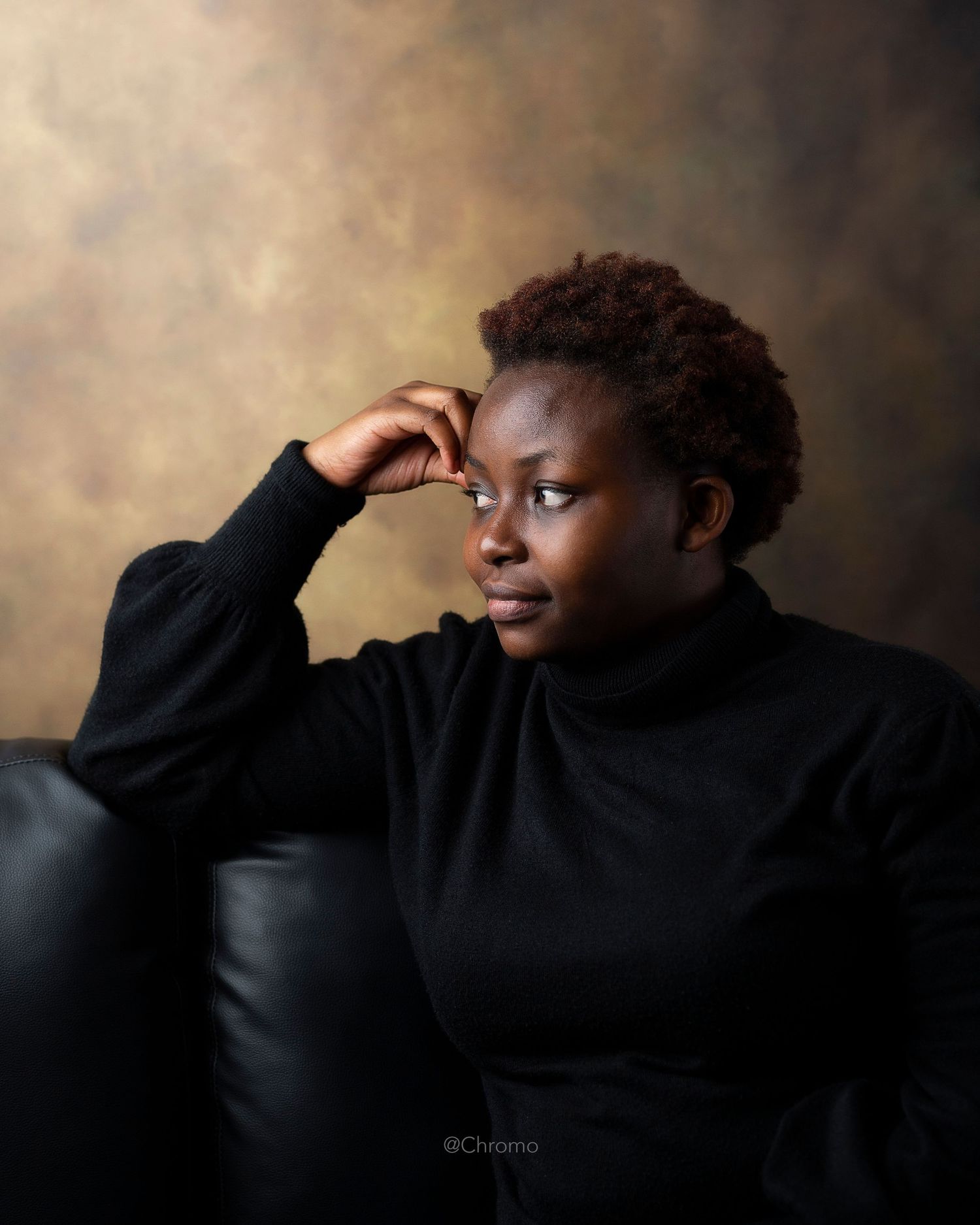 Portrait of person in black turtleneck sweater with thoughtful pose against brown backdrop.