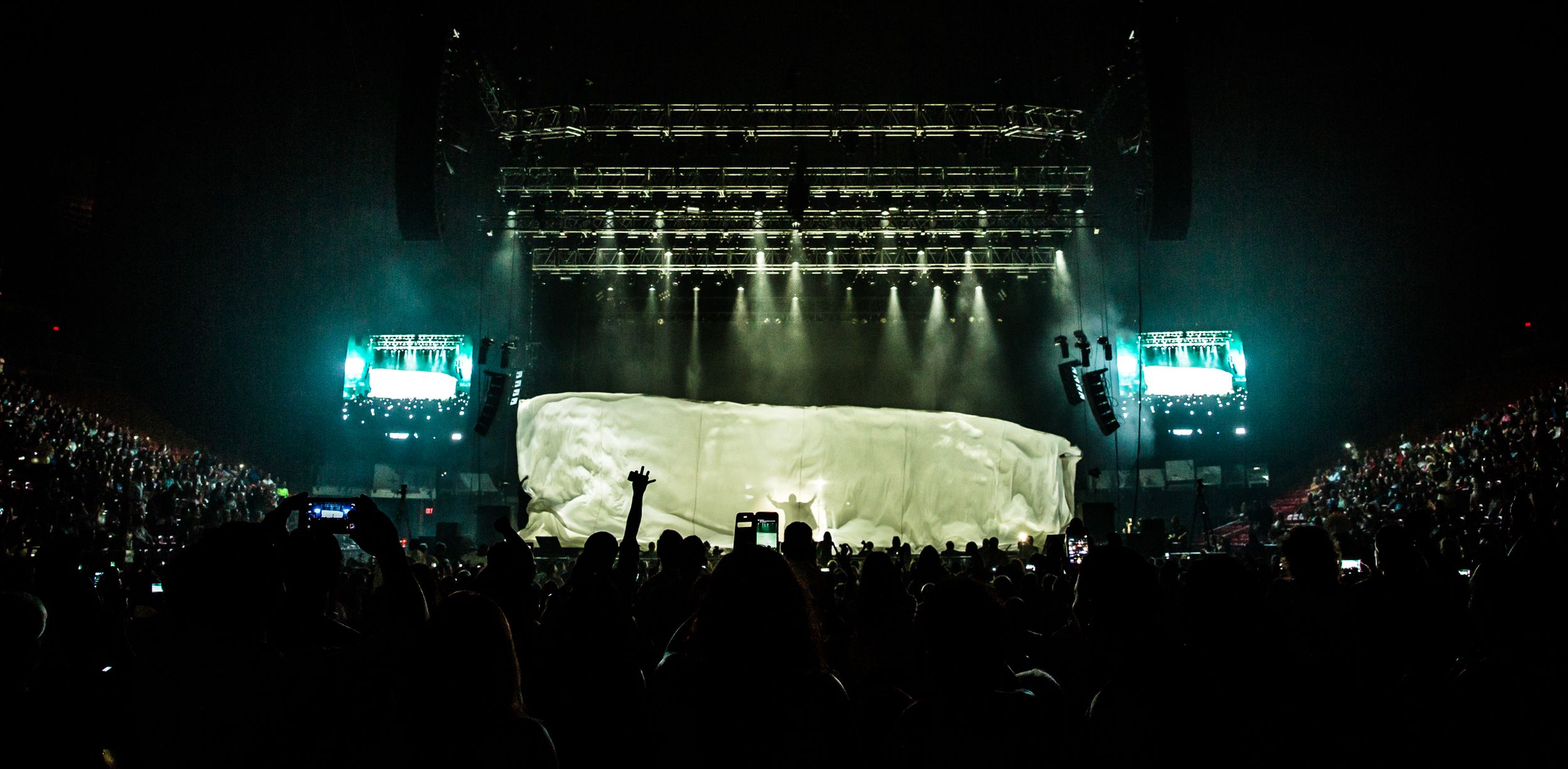 Concert venue with teal lighting and crowd silhouettes during a live performance.