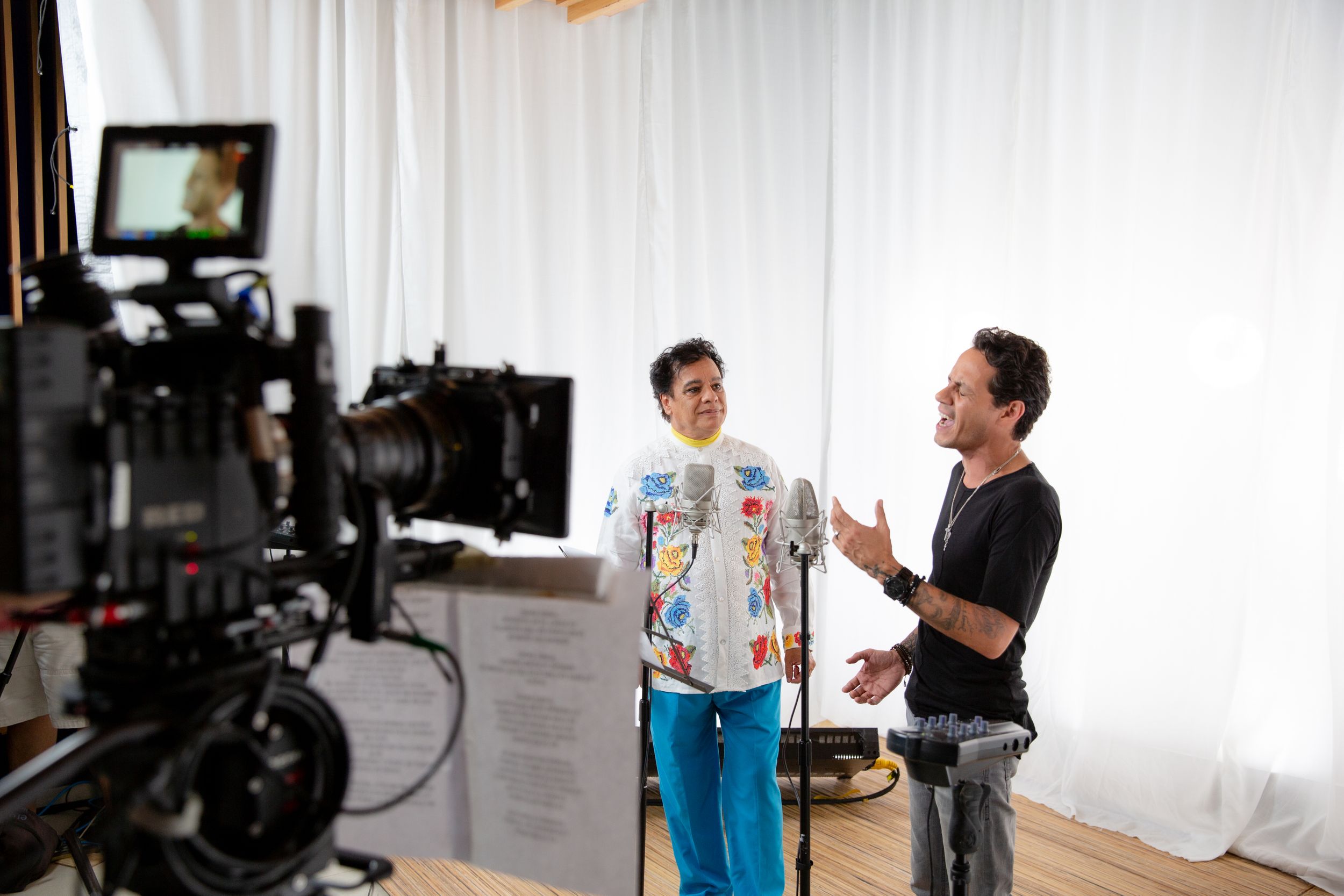 Behind the scenes filming setup with camera equipment and white studio backdrop.