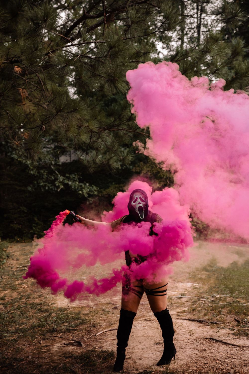 Artistic photo session with vibrant pink smoke effects in a wooded area.