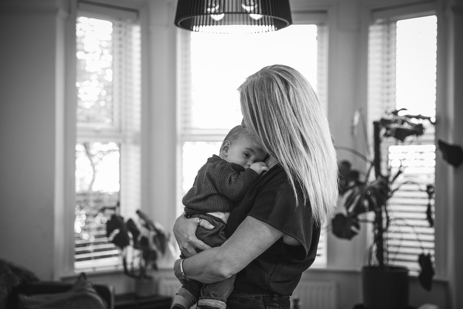 Black and white image capturing tender moment by window with natural light filtering through.