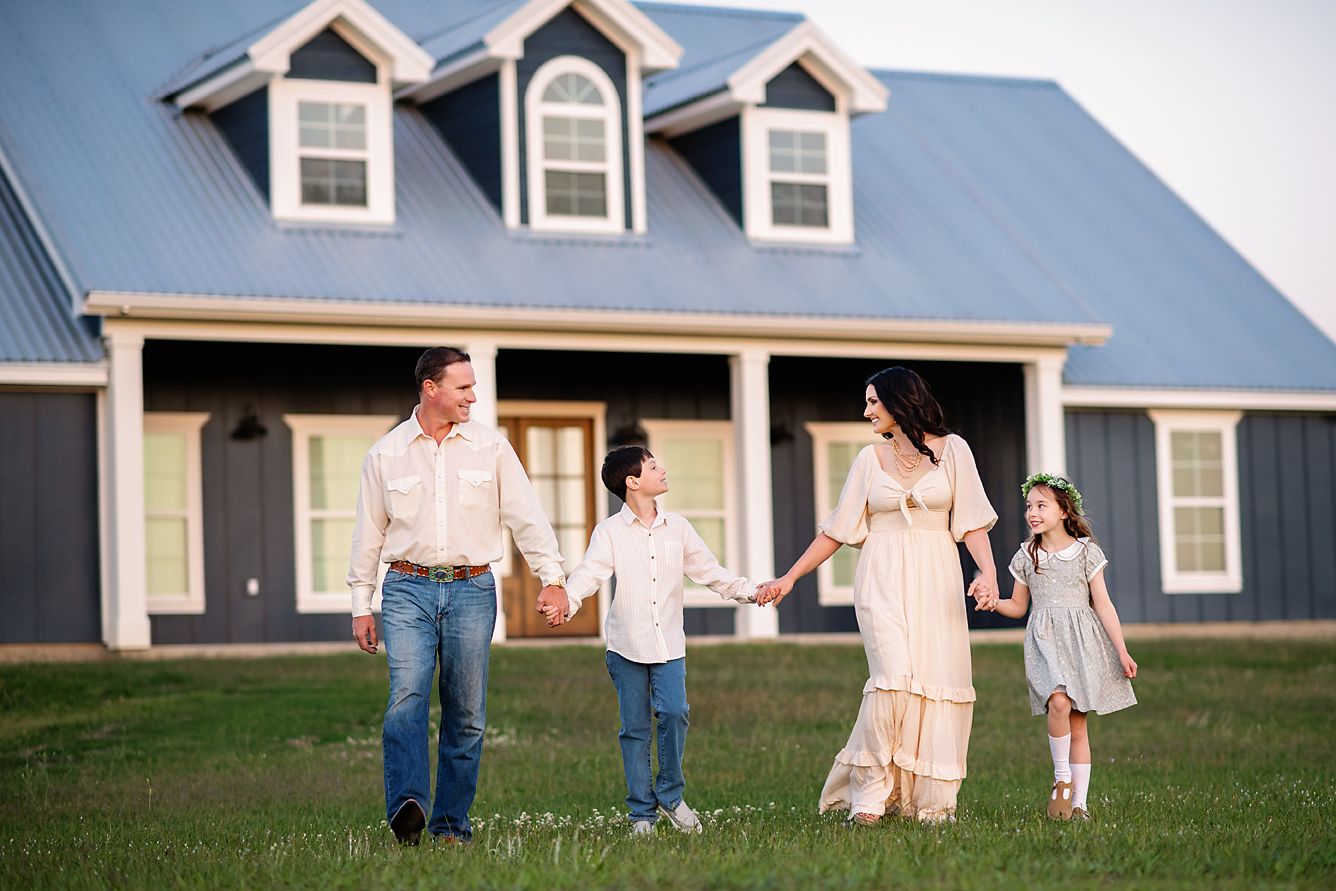 Happy family of four holding hands walking in front of a charming blue-roofed farmhouse.