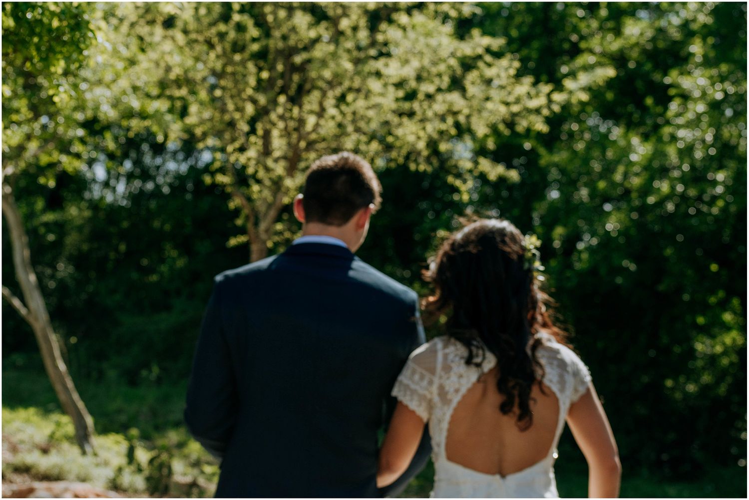 A silhouetted back view of a couple in wedding attire against a sunlit natural backdrop.
