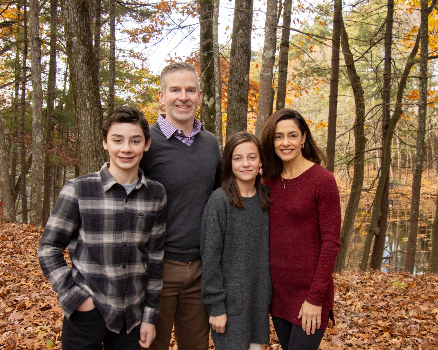 Family of four poses together among fall foliage in wooded setting.