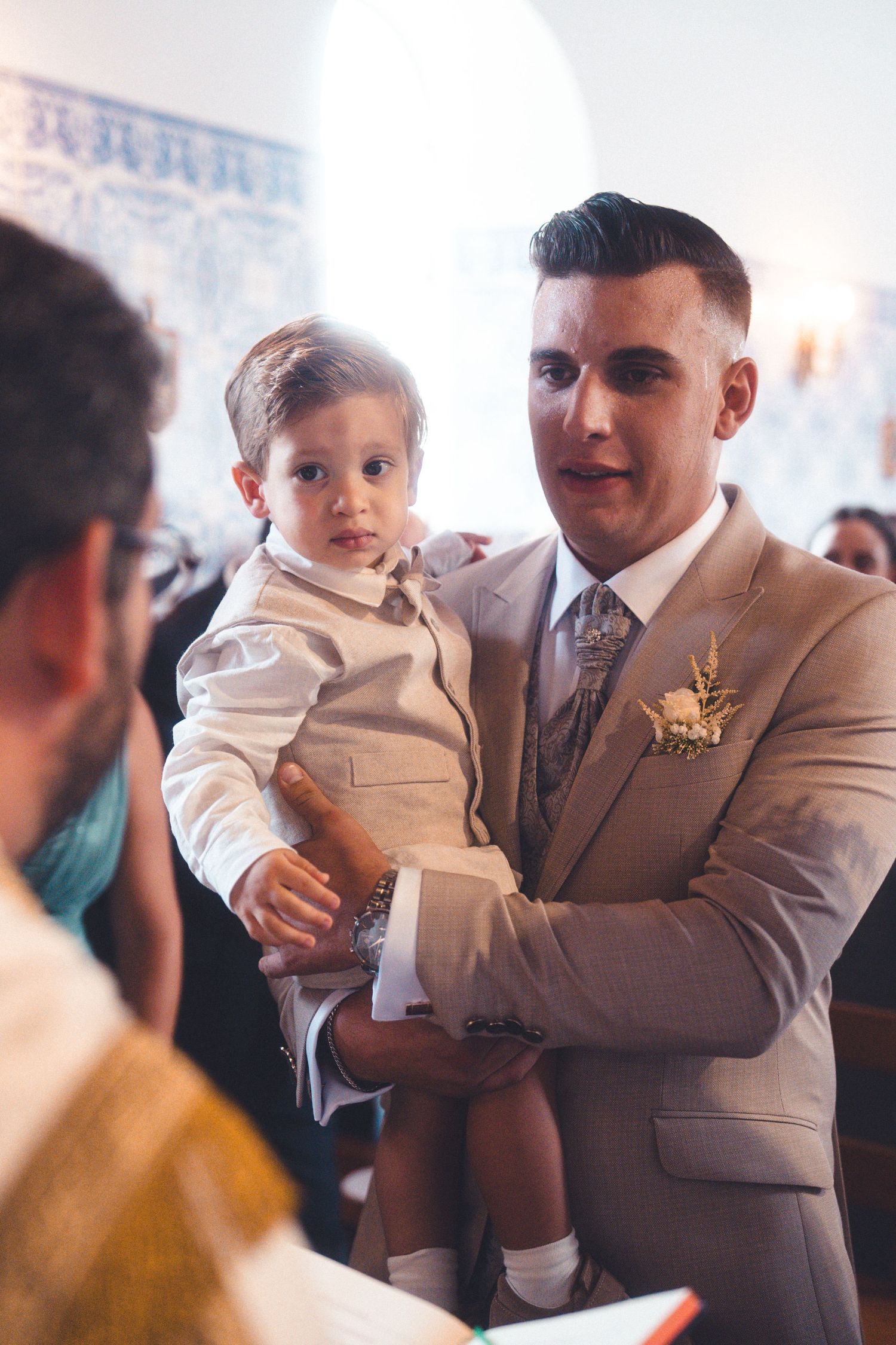 A small child in formal attire is held during a wedding celebration.