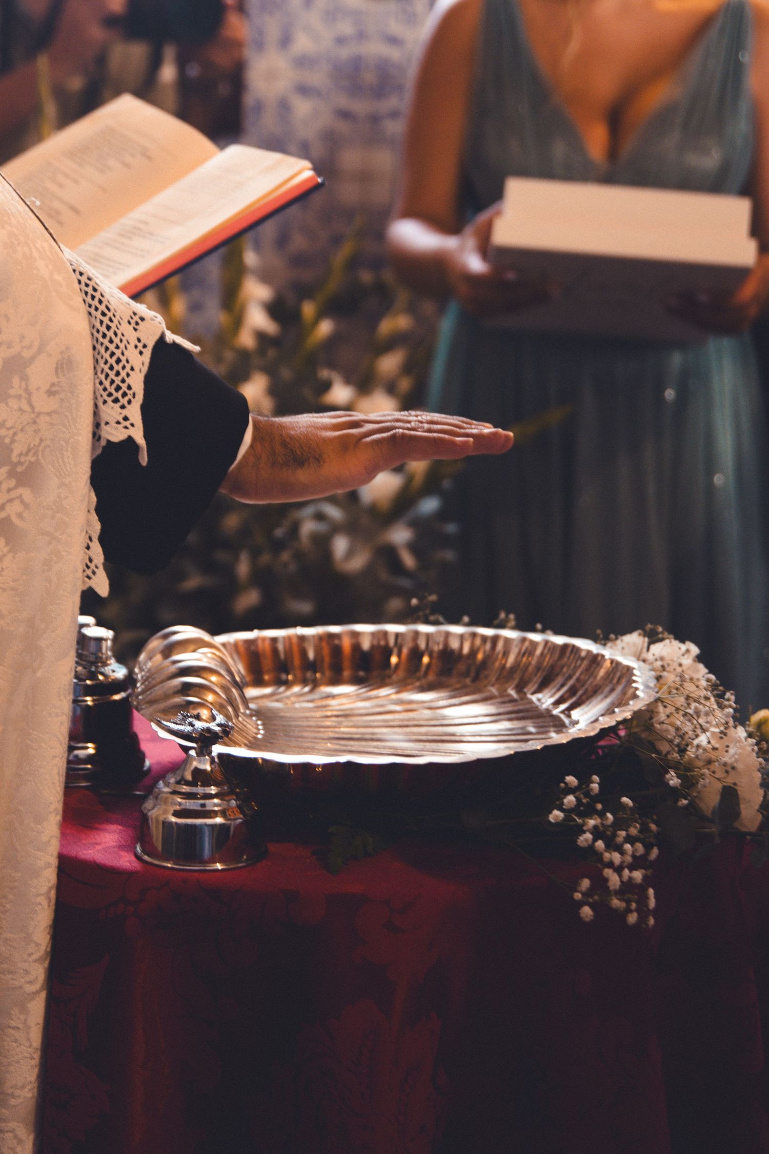 A silver baptismal font decorated with flowers and lace during a religious ceremony.