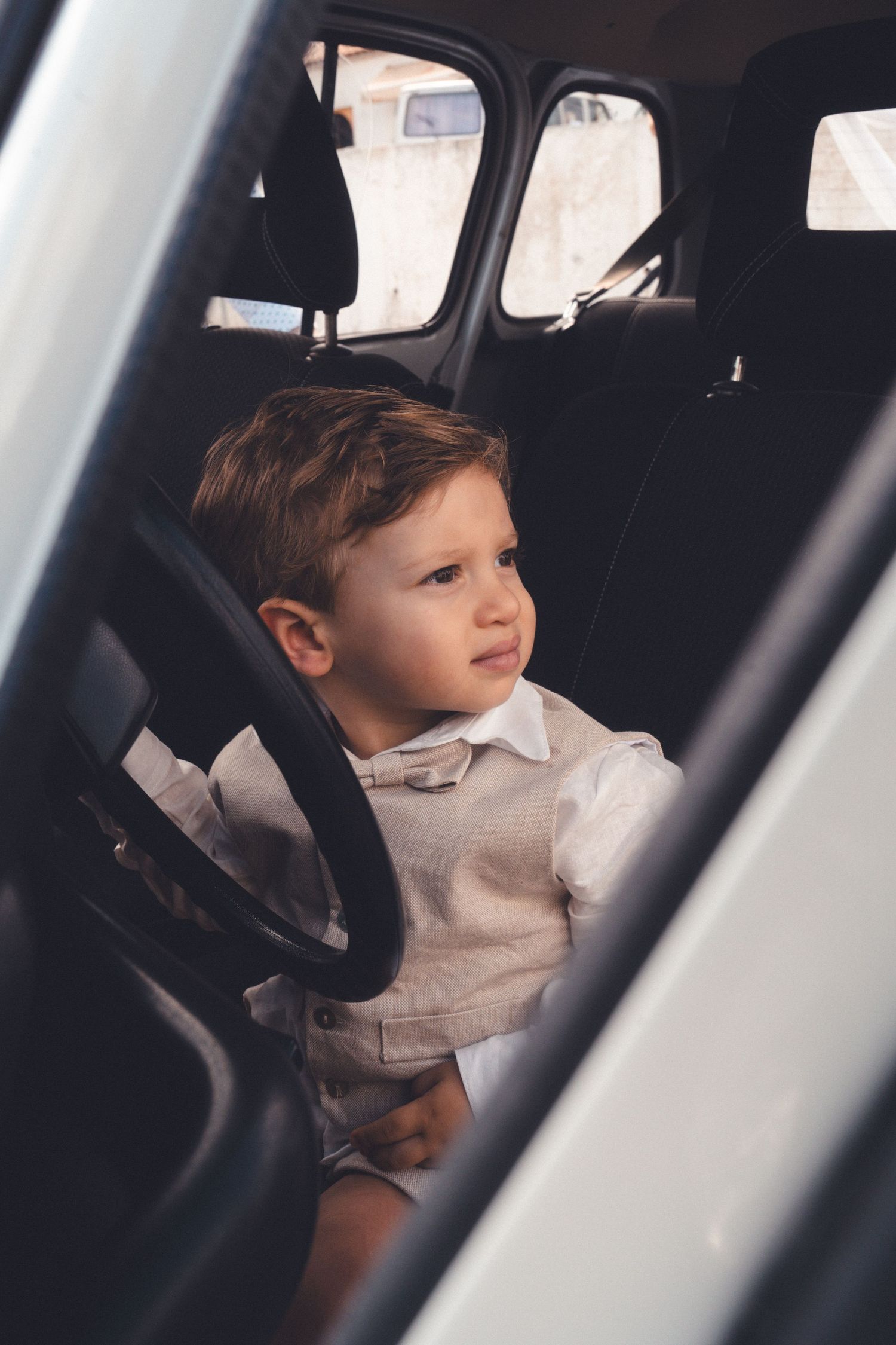Young child in formal attire sits in a car seat looking to the side.