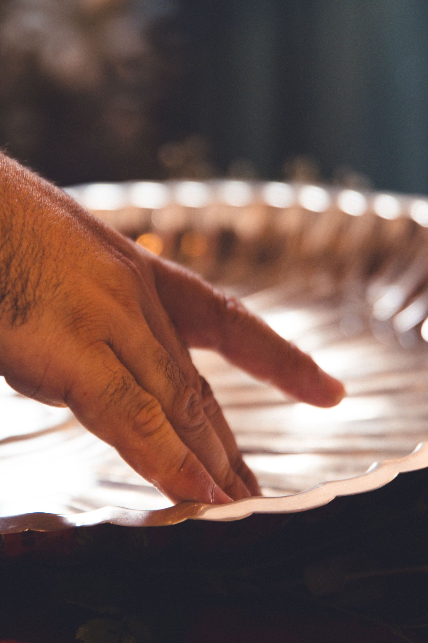 Close-up of a hand touching a silver baptismal basin during a ceremony.