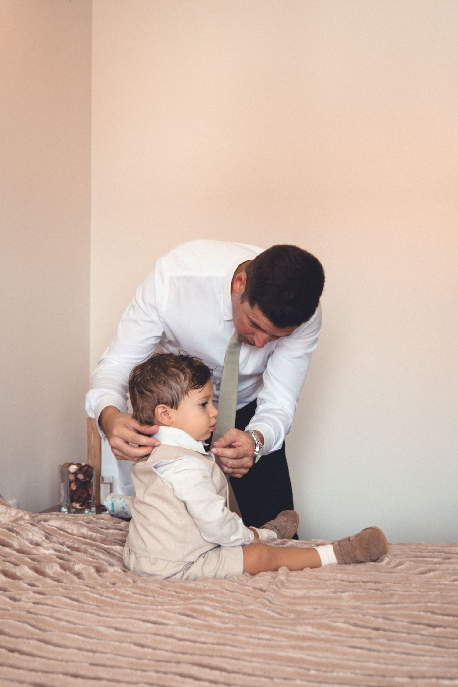 A caregiver helps dress a young child in formal attire on a bed.