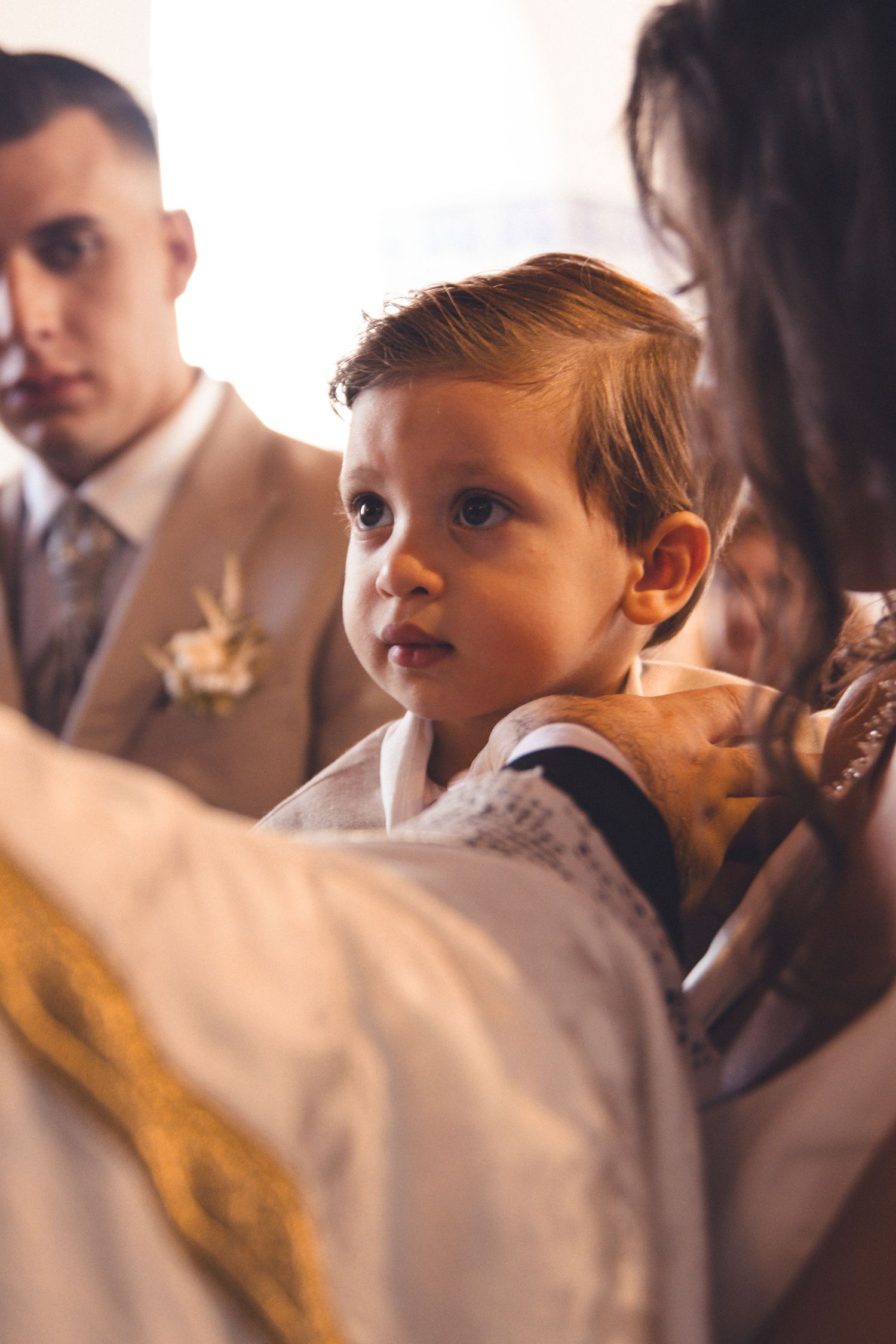 A young child in white formal attire looks on during a ceremonial event.