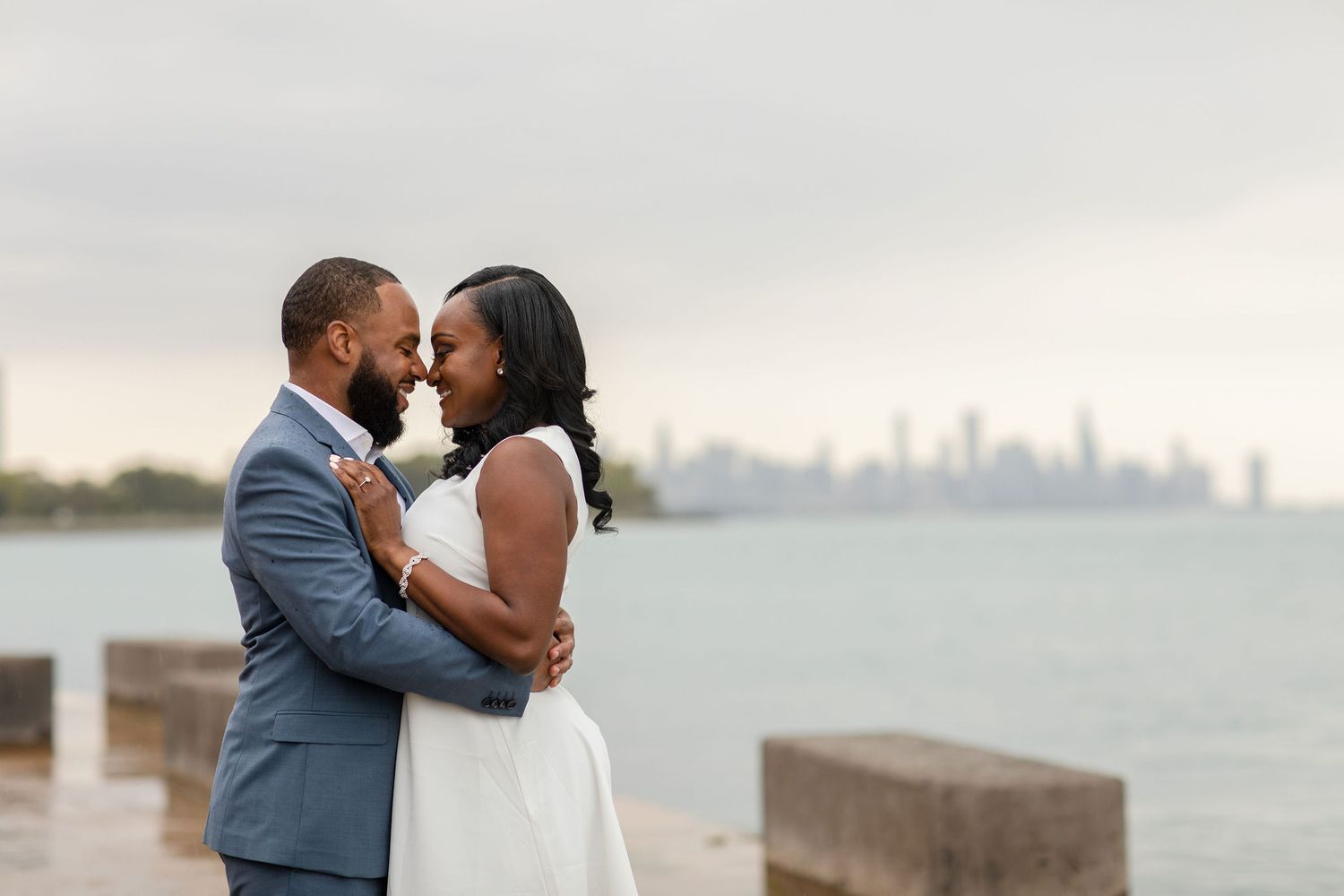 A couple embraces with a city skyline visible across the water behind them.