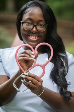 Person wearing glasses holds pink heart-shaped medical equipment while smiling warmly.