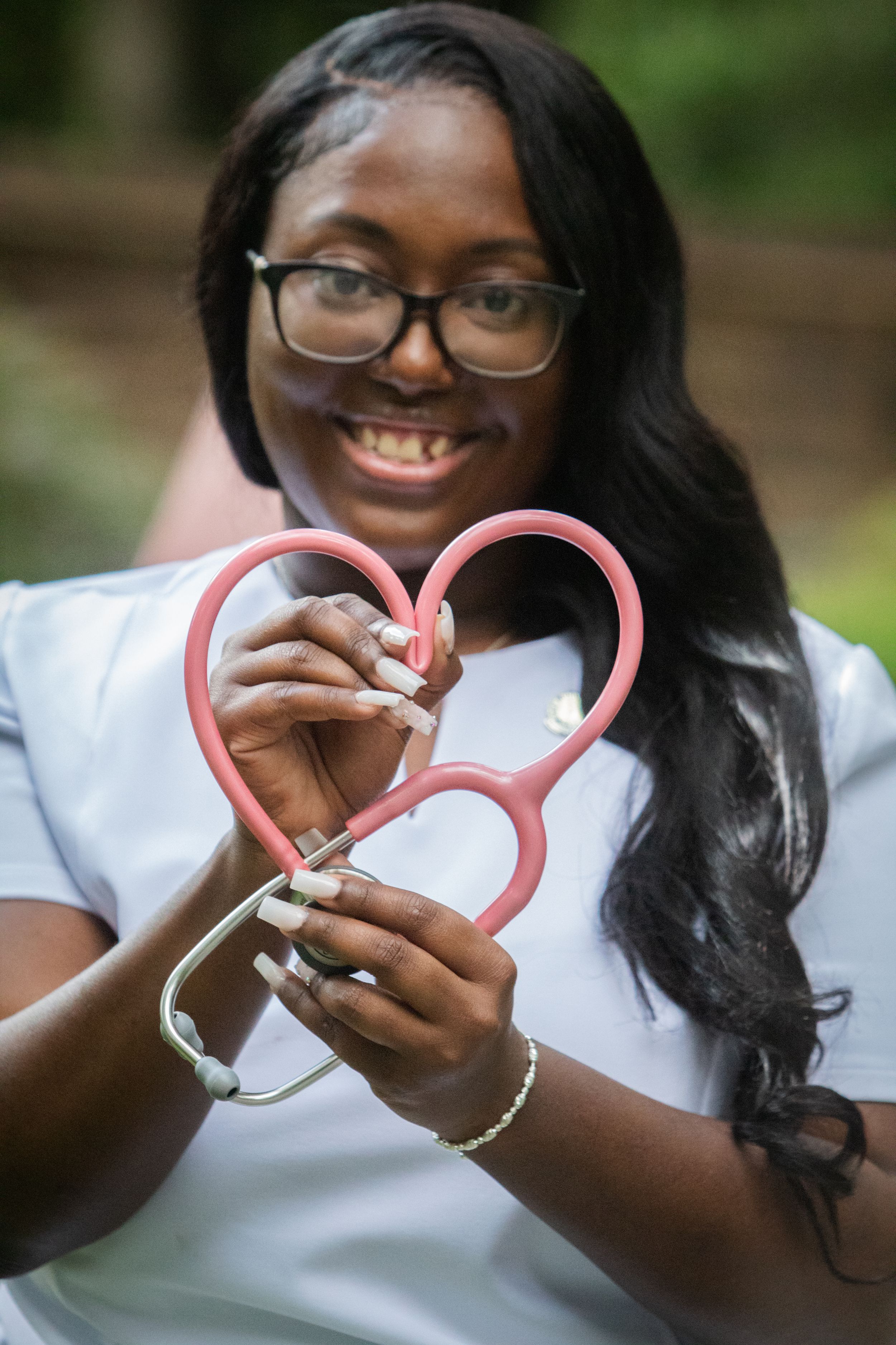 Person wearing glasses holds pink heart-shaped medical equipment while smiling warmly.
