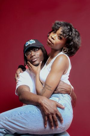 Couple in casual attire embracing in an intimate portrait against a red background.