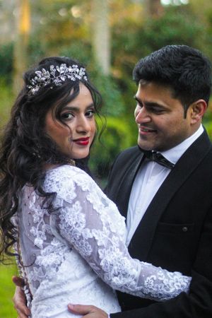 Wedding couple in white lace dress and black suit posing in garden setting.