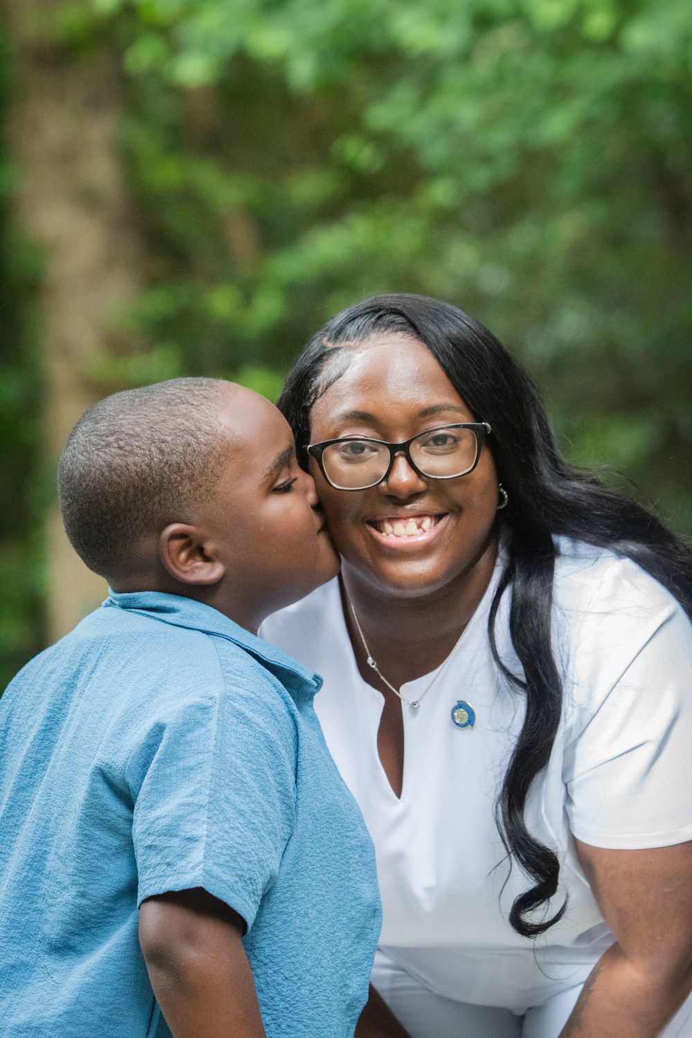 Sweet moment captured between parent and child outdoors with natural green background.