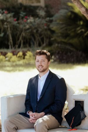Professional in navy blazer and khakis sits outdoors in natural lighting.