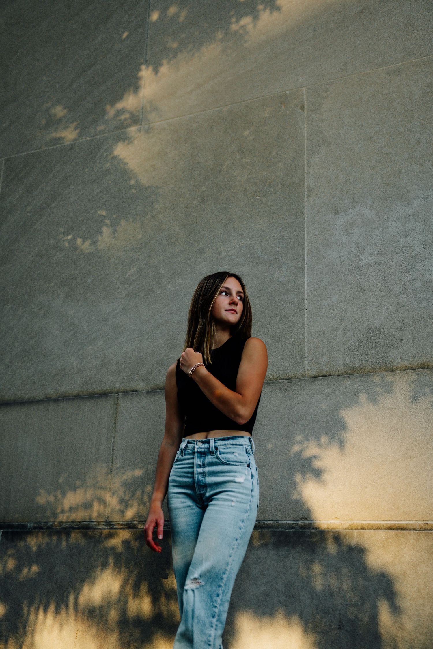 Urban portrait of someone in casual outfit against concrete wall with dramatic shadow play.
