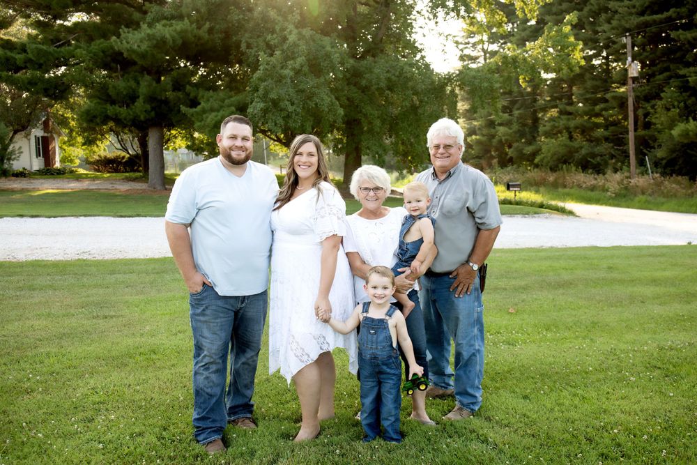 Multi-generational family poses together for portrait on grass in summer setting.