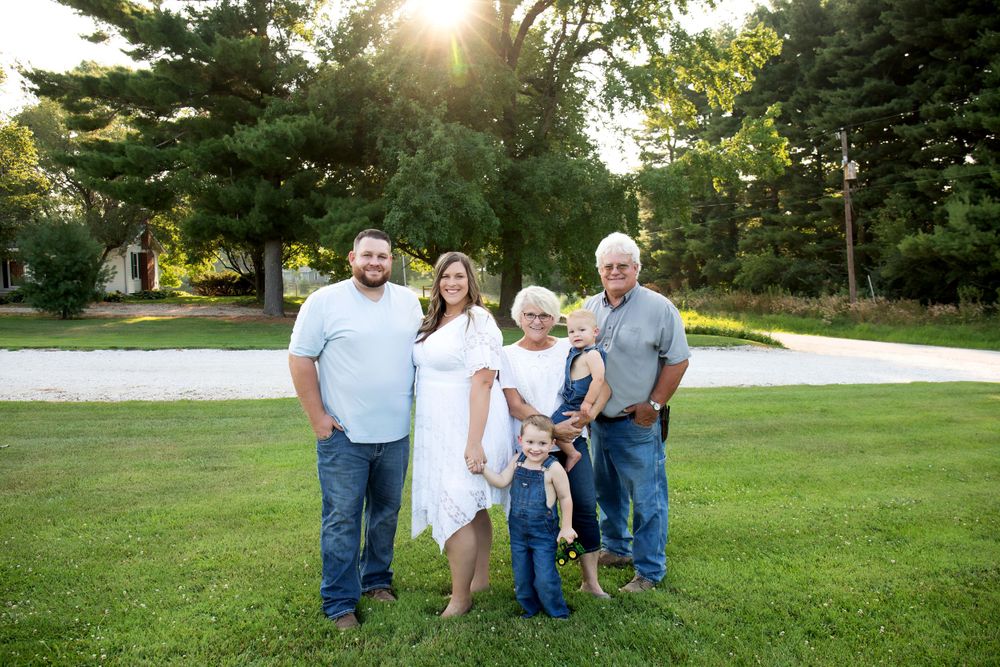 Multigenerational family portrait taken outdoors at sunset with green trees in the background.