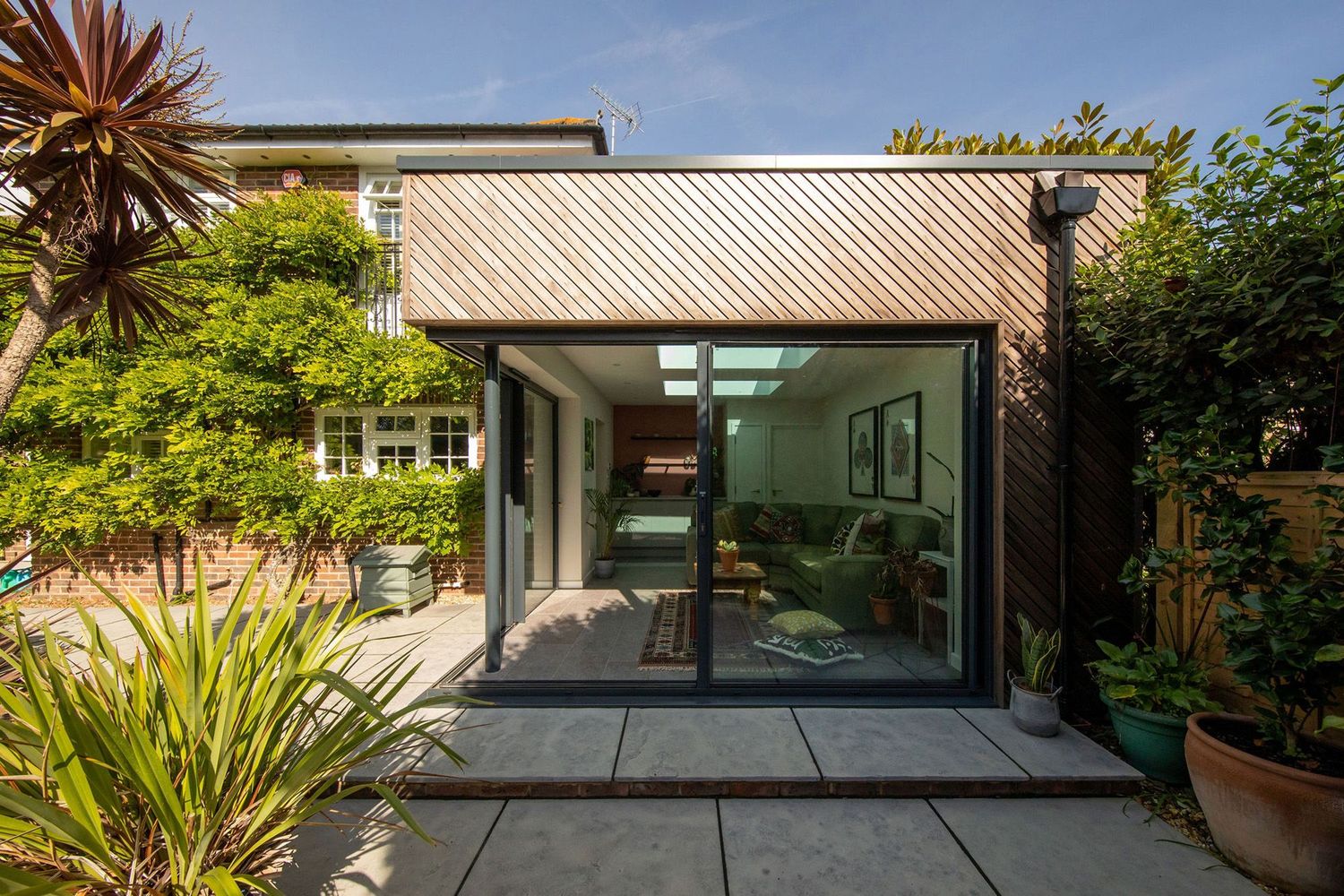 Modern garden studio with glass sliding doors and wood-clad exterior surrounded by tropical plants.