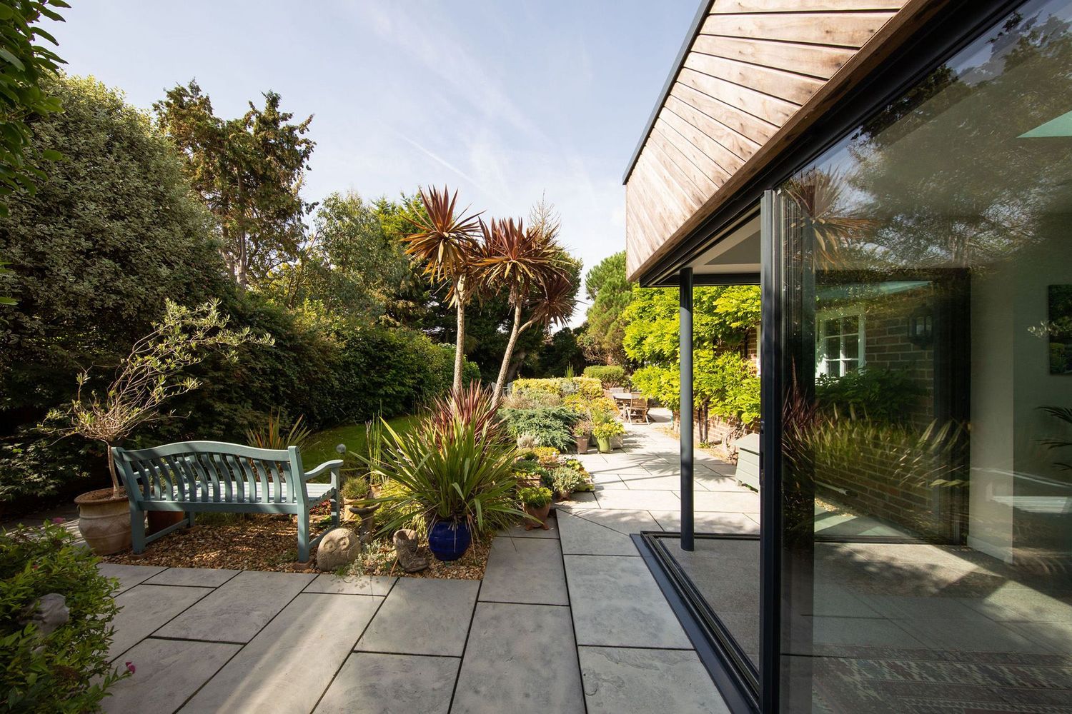 Contemporary garden patio with slate tiles, tropical plants, and sleek glass sliding doors.