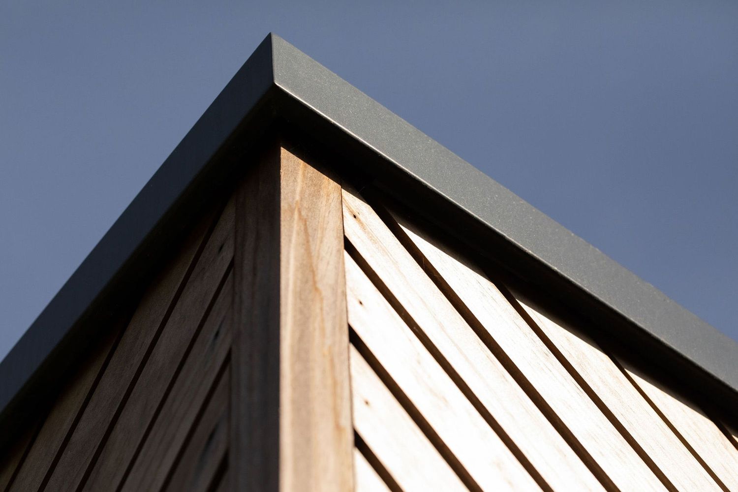 Architectural detail of a wooden and black metal roof corner against a dark sky.