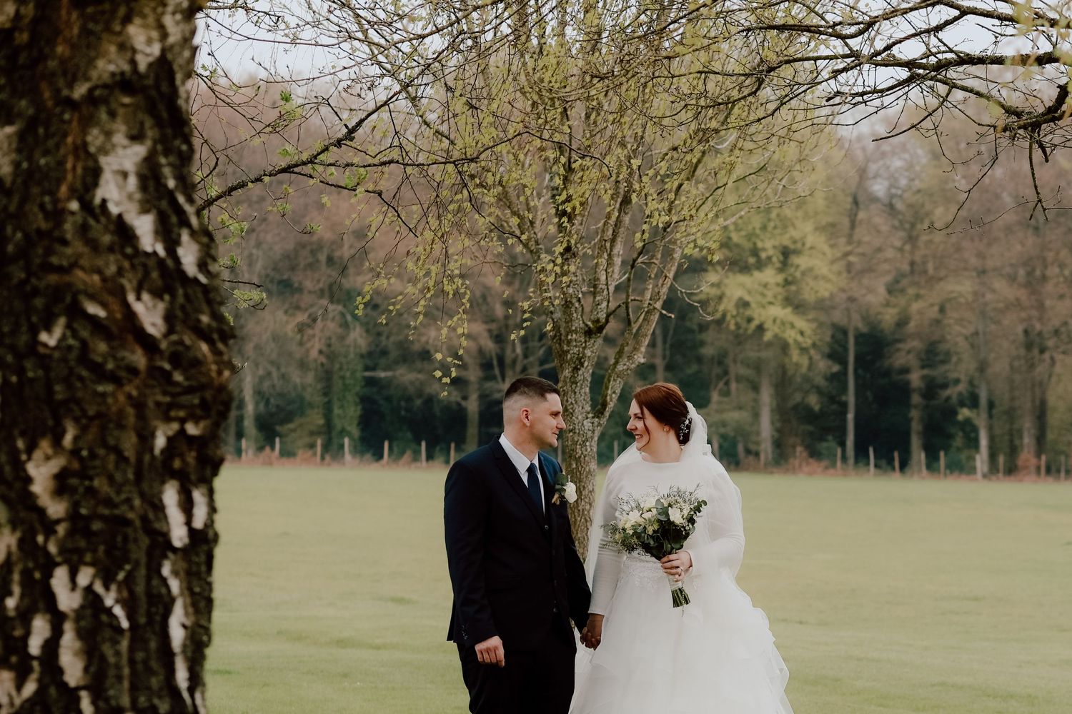 A romantic winter wedding photo captured between birch trees on a grassy field.
