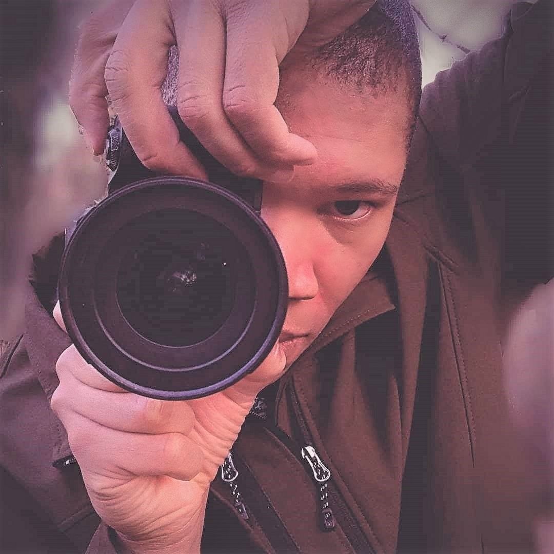 A photographer points his camera at a subject, his lens on full display.