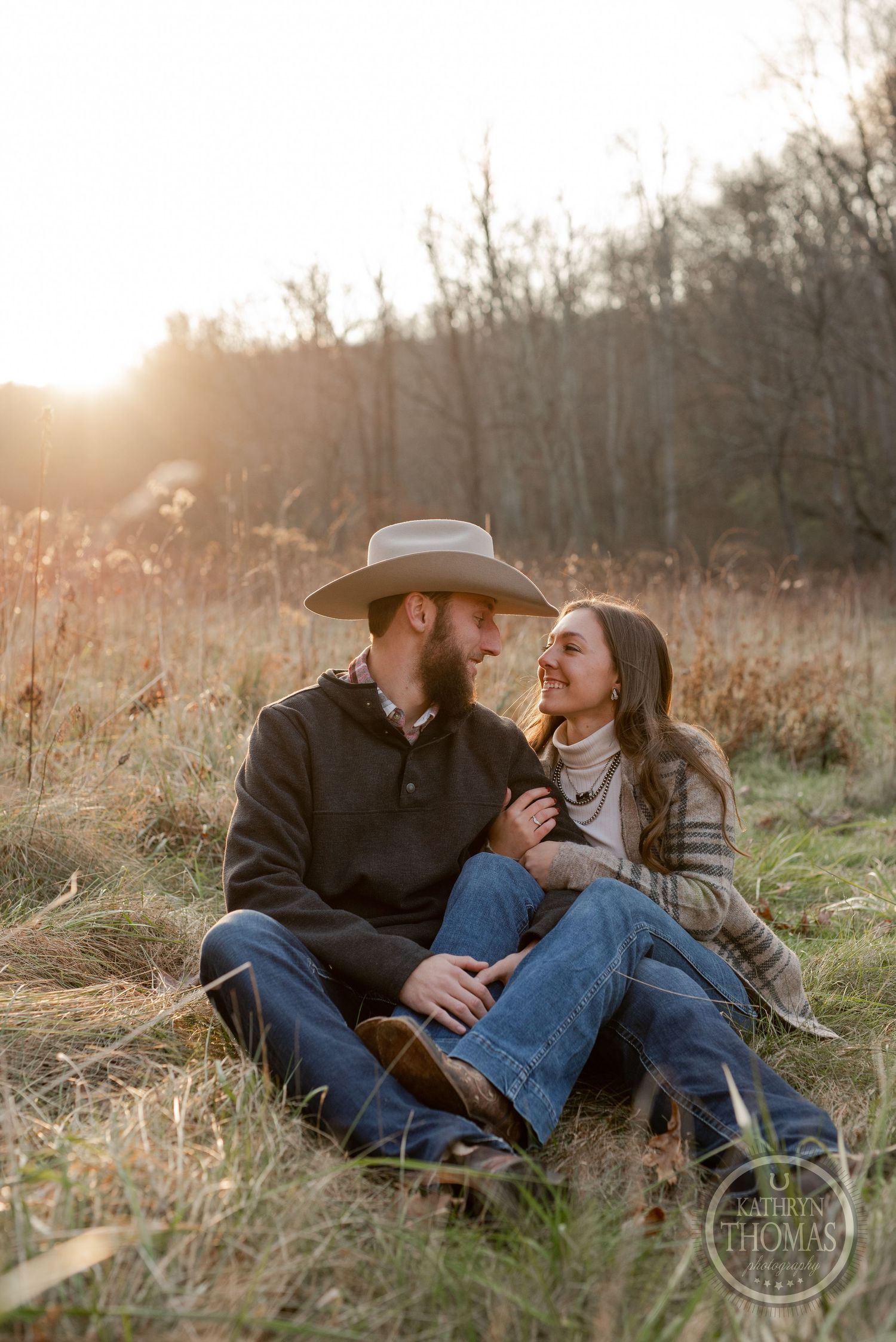 A couple shares a candid moment while sitting in tall grass during golden hour.