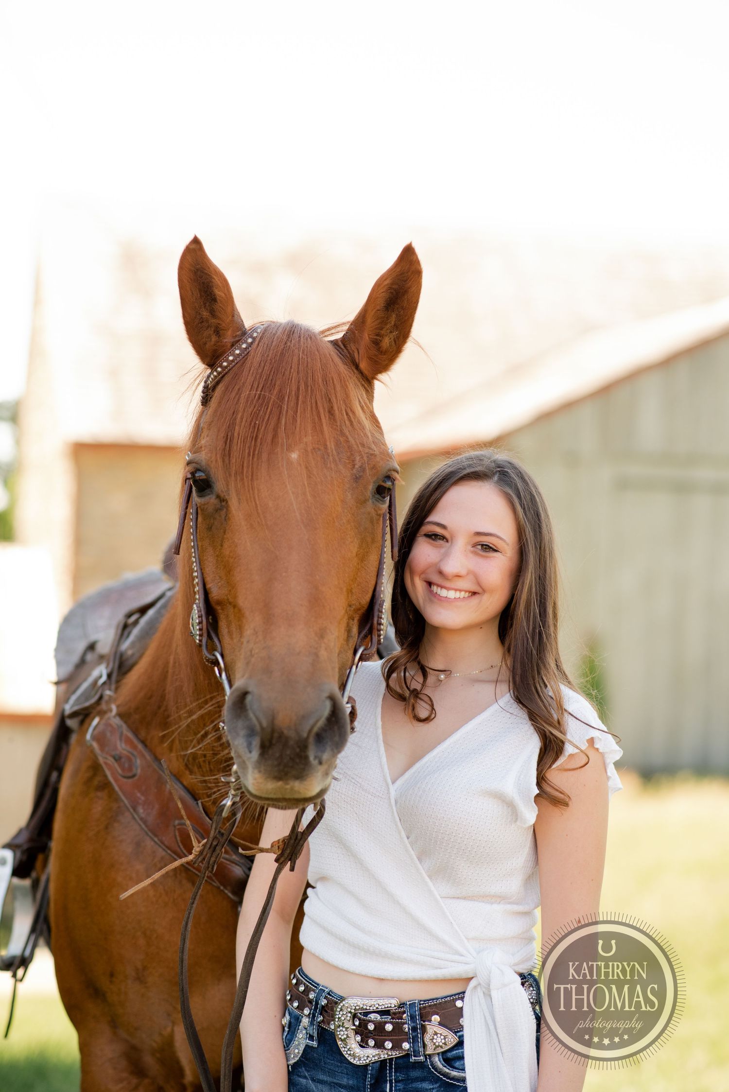 A close-up portrait of a chestnut horse and a woman in casual attire against a barn backdrop.