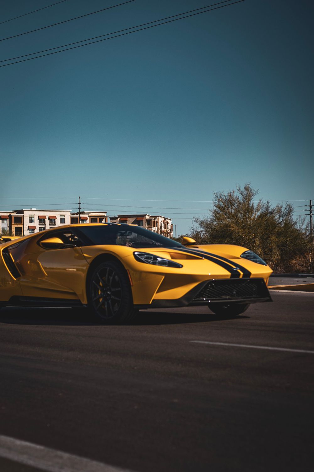 Yellow Ford GT supercar parked on the street with modern buildings in the background.