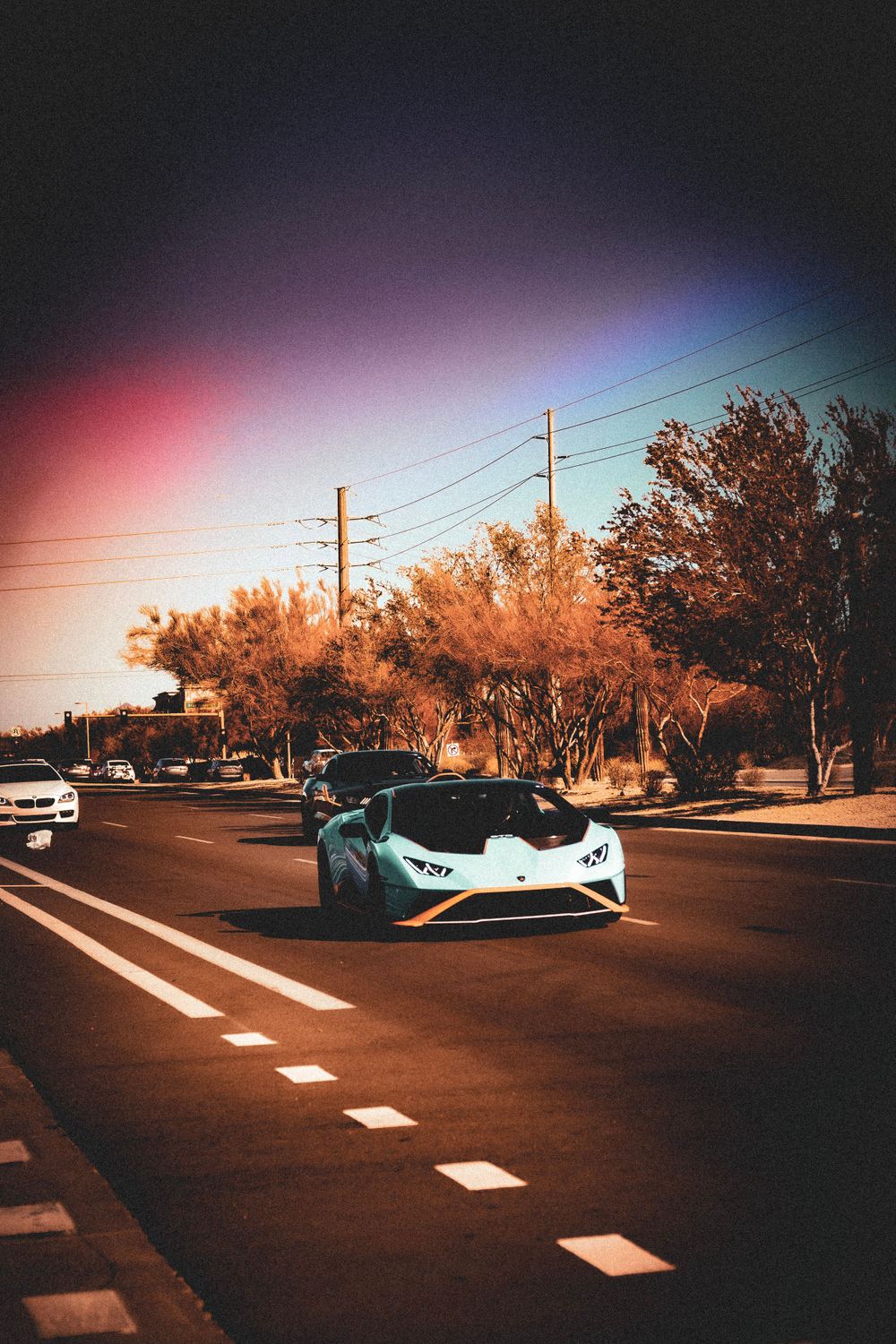 White supercar driving on road during sunset with power lines and trees in background.