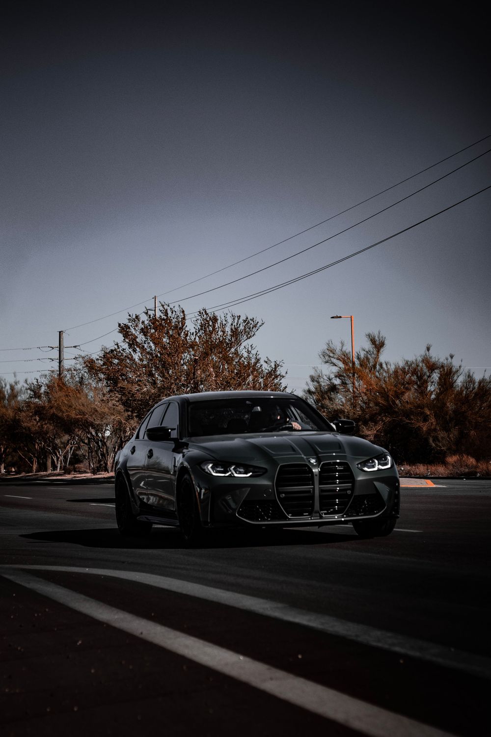 Black BMW M4 with distinctive large grille photographed against moody sky and power lines.