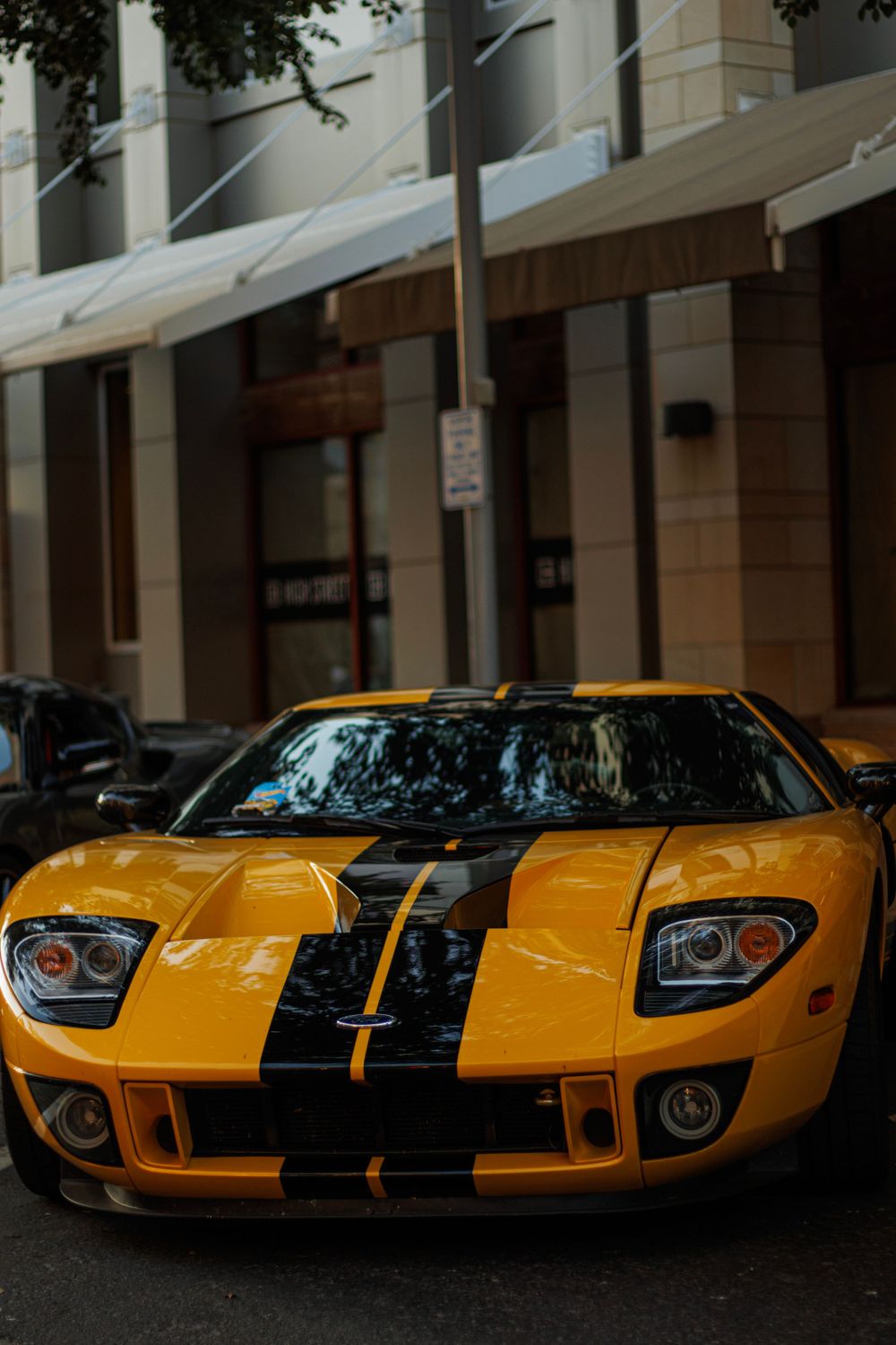 Yellow Ford GT with black racing stripes parked on city street showing iconic supercar design.