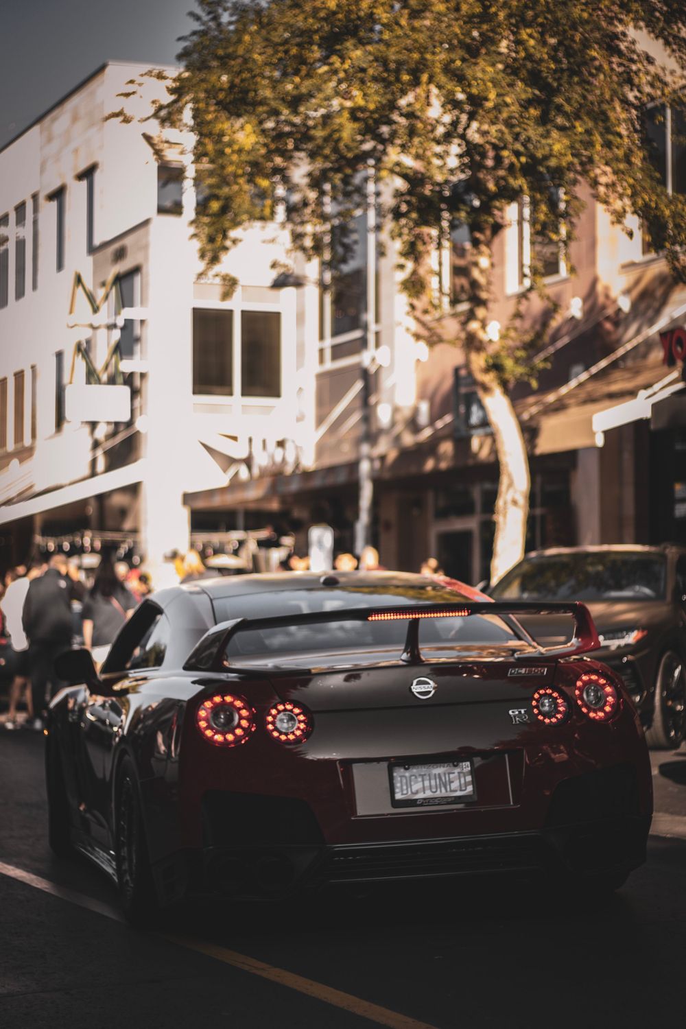 Black Nissan GT-R with glowing taillights parked on city street under autumn trees.