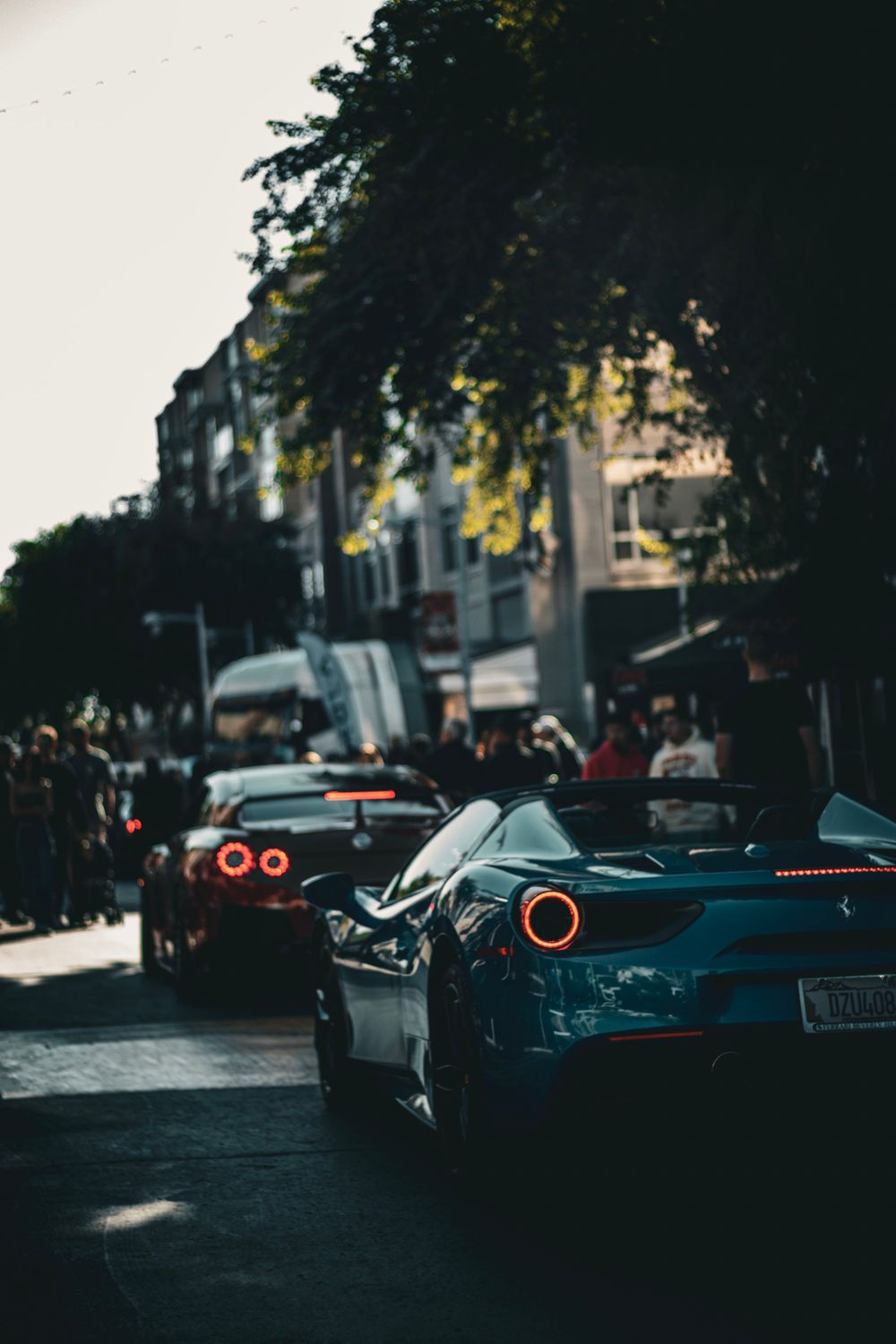 Line of sports cars parked on urban street at dusk with buildings and trees in background.