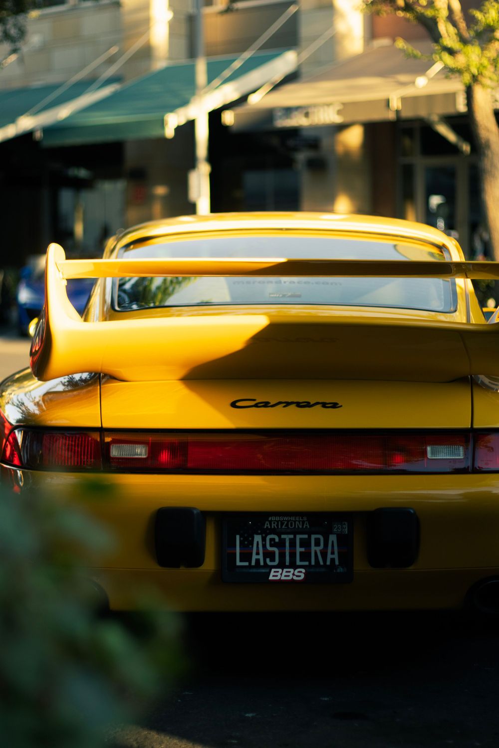 Rear view of a yellow Porsche 911 Carrera with distinctive taillights and custom license plate at sunset.