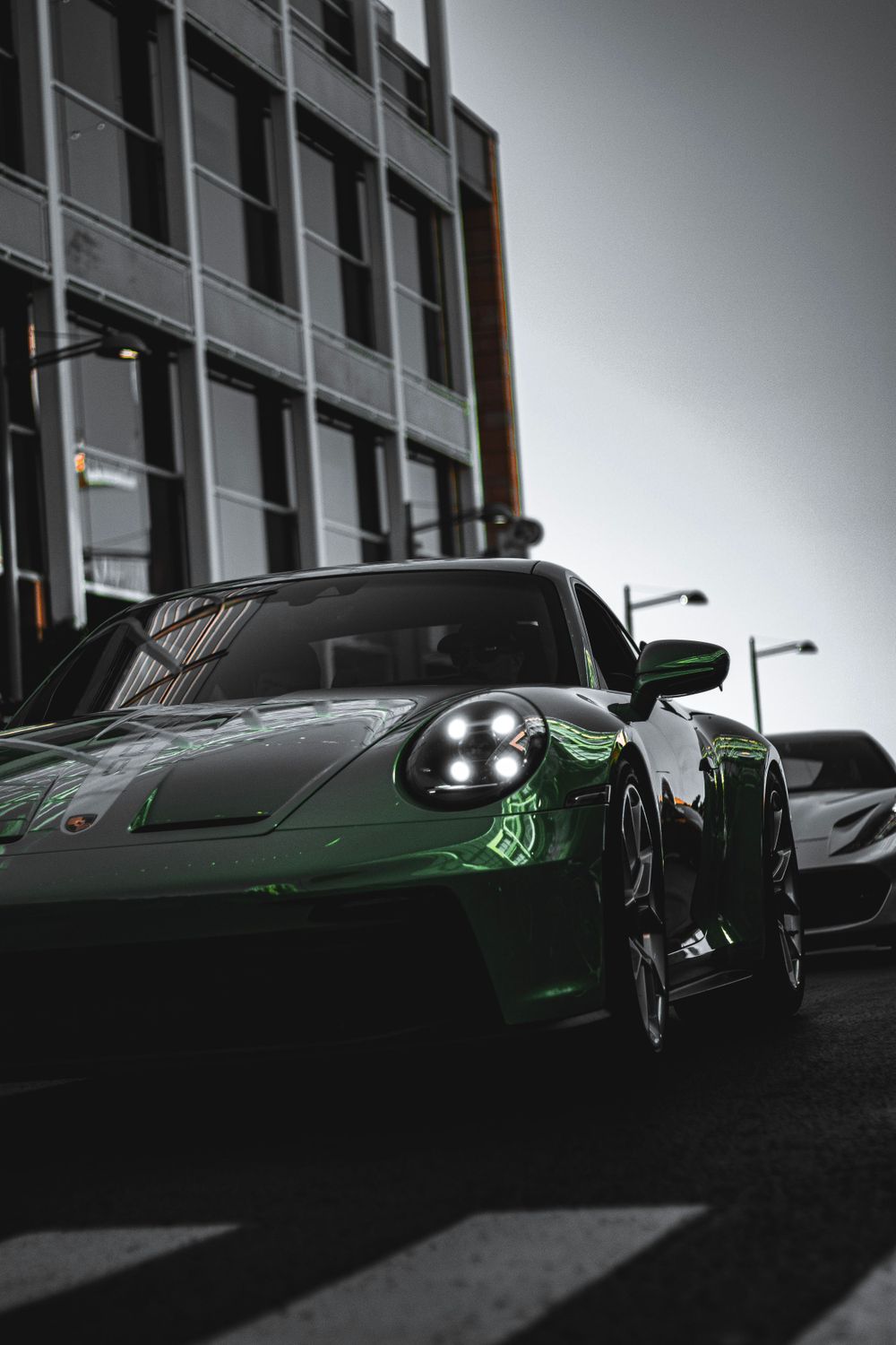 Dark green Porsche 911 photographed from a low angle against an industrial building backdrop.