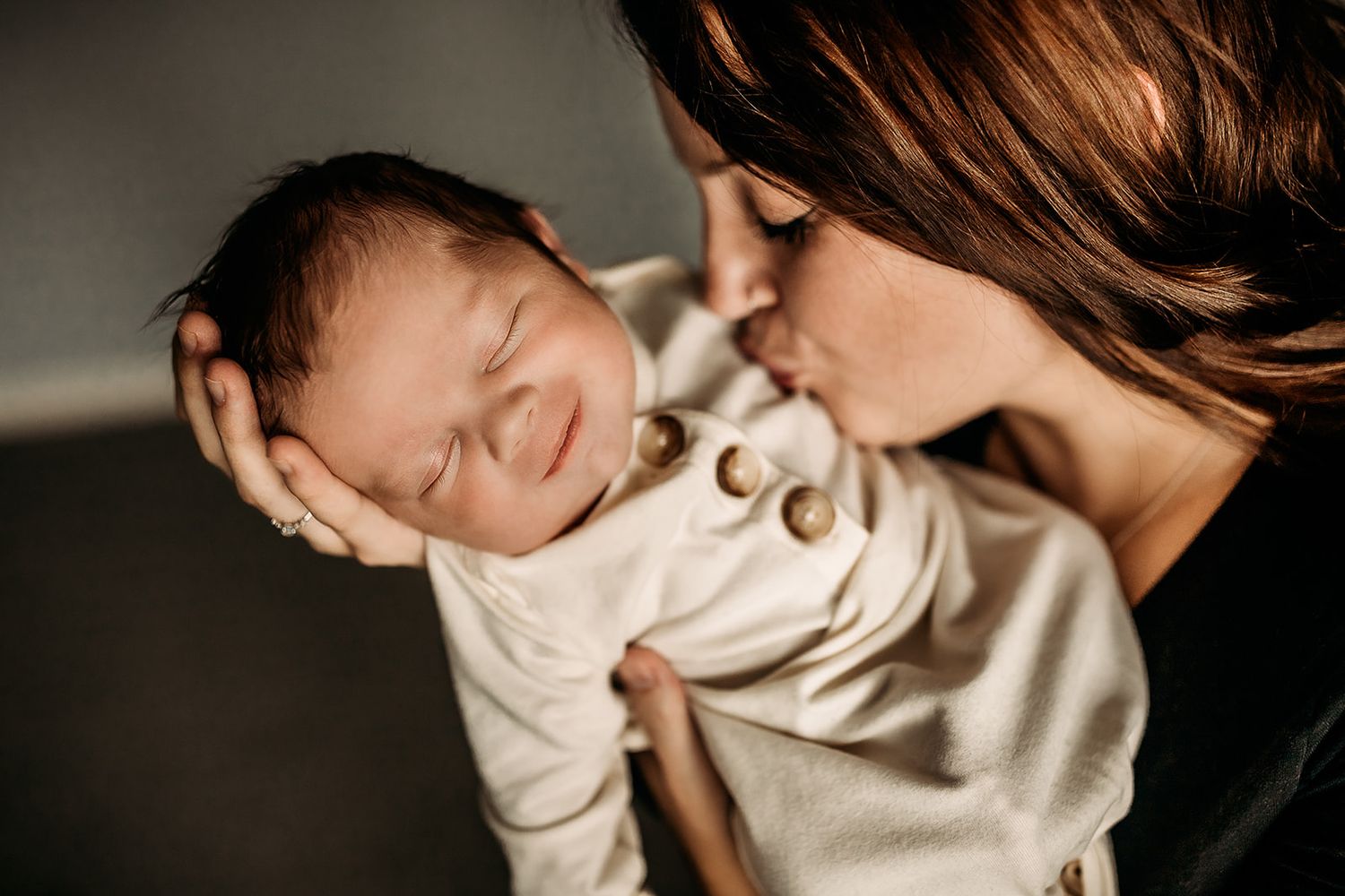 A mother leans over to kiss her smiling baby boy.
