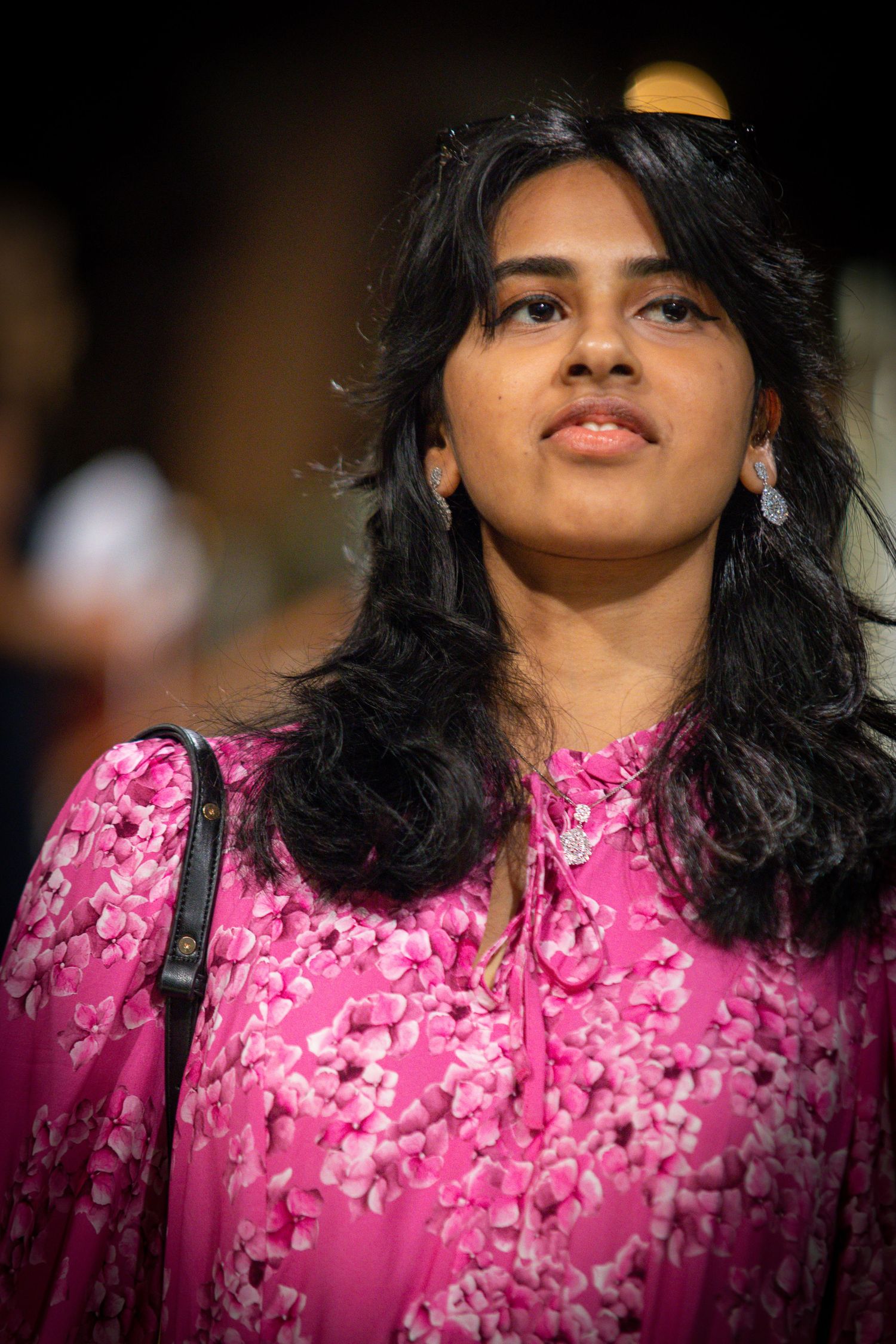 Young South Asian woman in a pink floral dress with dangling earrings at an evening event.