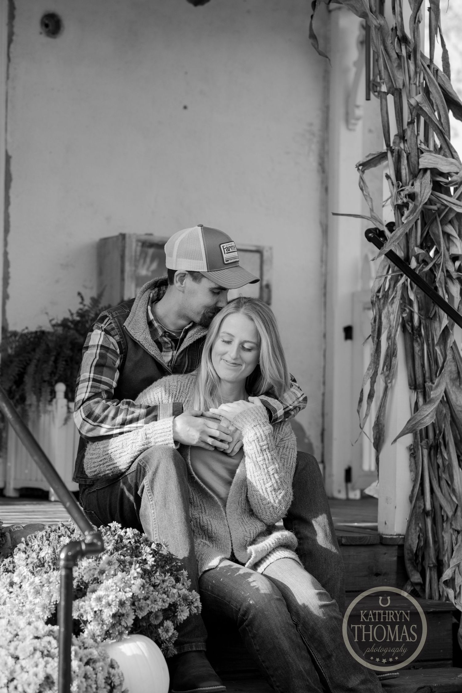 Intimate black and white portrait of a couple relaxing on porch steps with autumn decor.