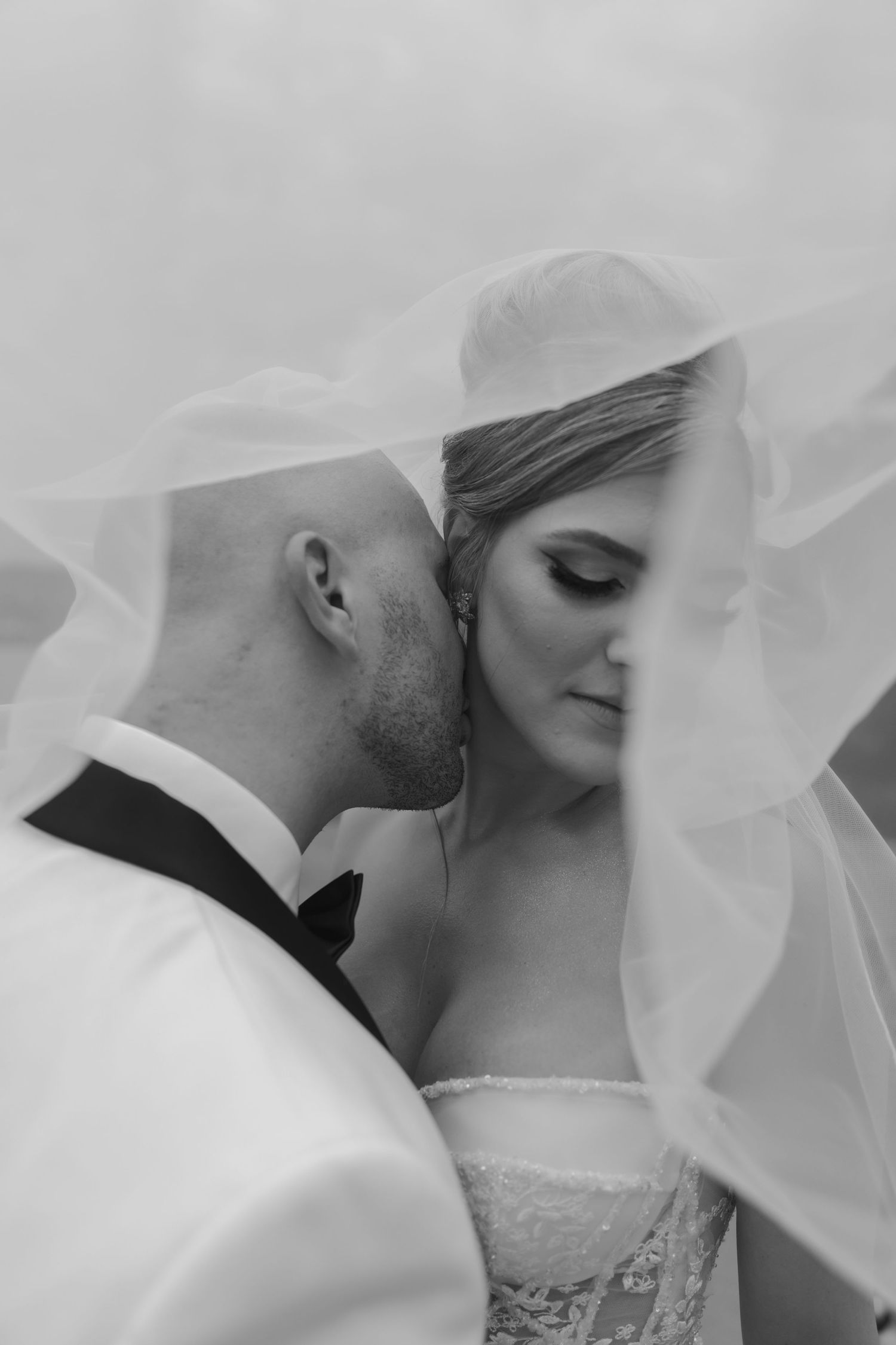 An intimate black and white portrait through a delicate veil capturing a romantic wedding moment.