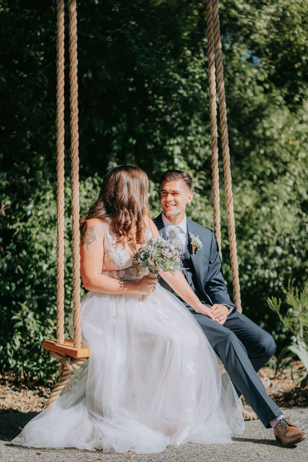 Couple sharing a sweet moment on a rustic wooden swing in a garden setting.