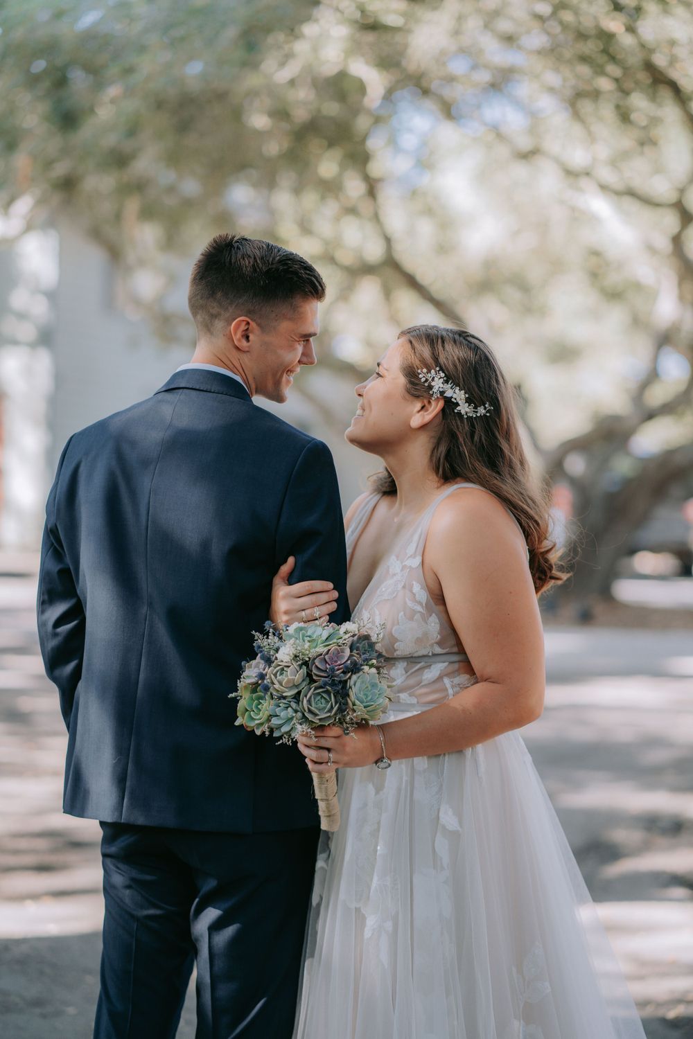 A romantic moment captured between a couple in wedding attire under shaded trees.