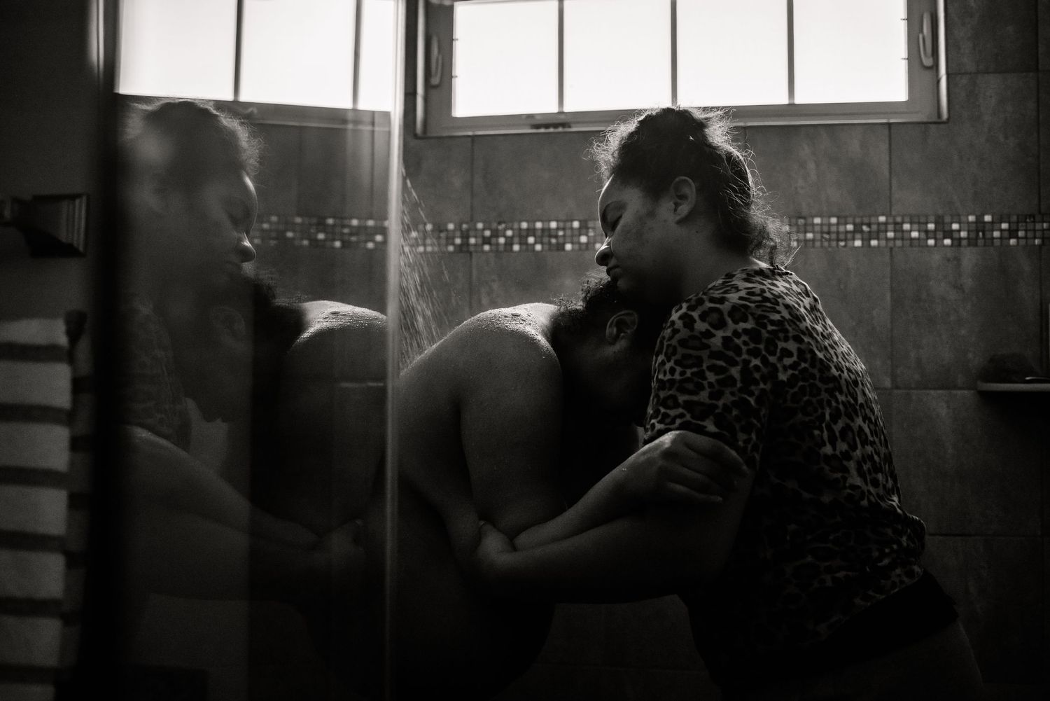 A woman and her doula standing in a shower holding each other as the shower water hits the woman's back